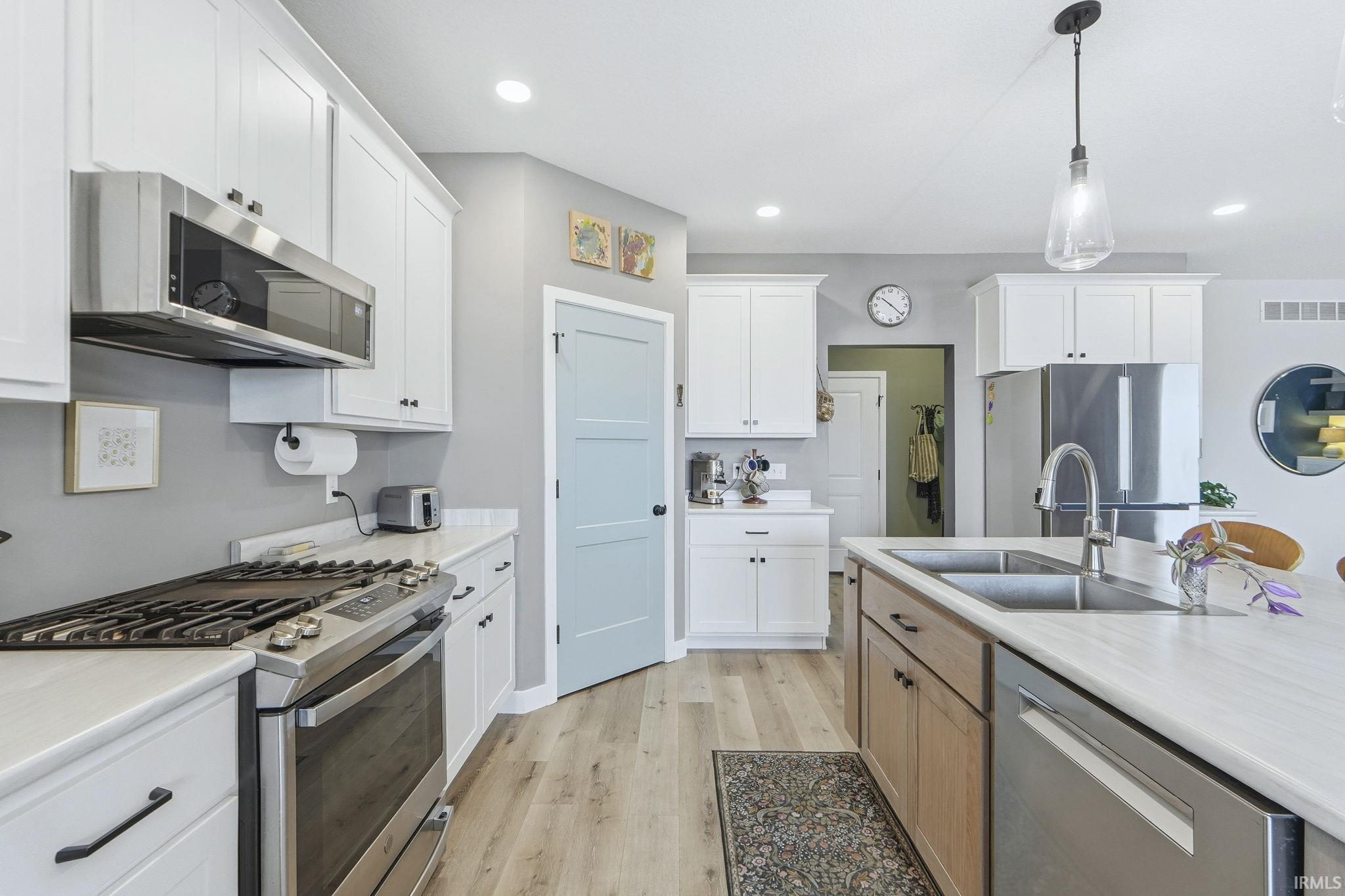 Dual tone kitchen featuring stainless steel appliances, hanging light fixtures, two tone cabinetry, and light wood-style flooring