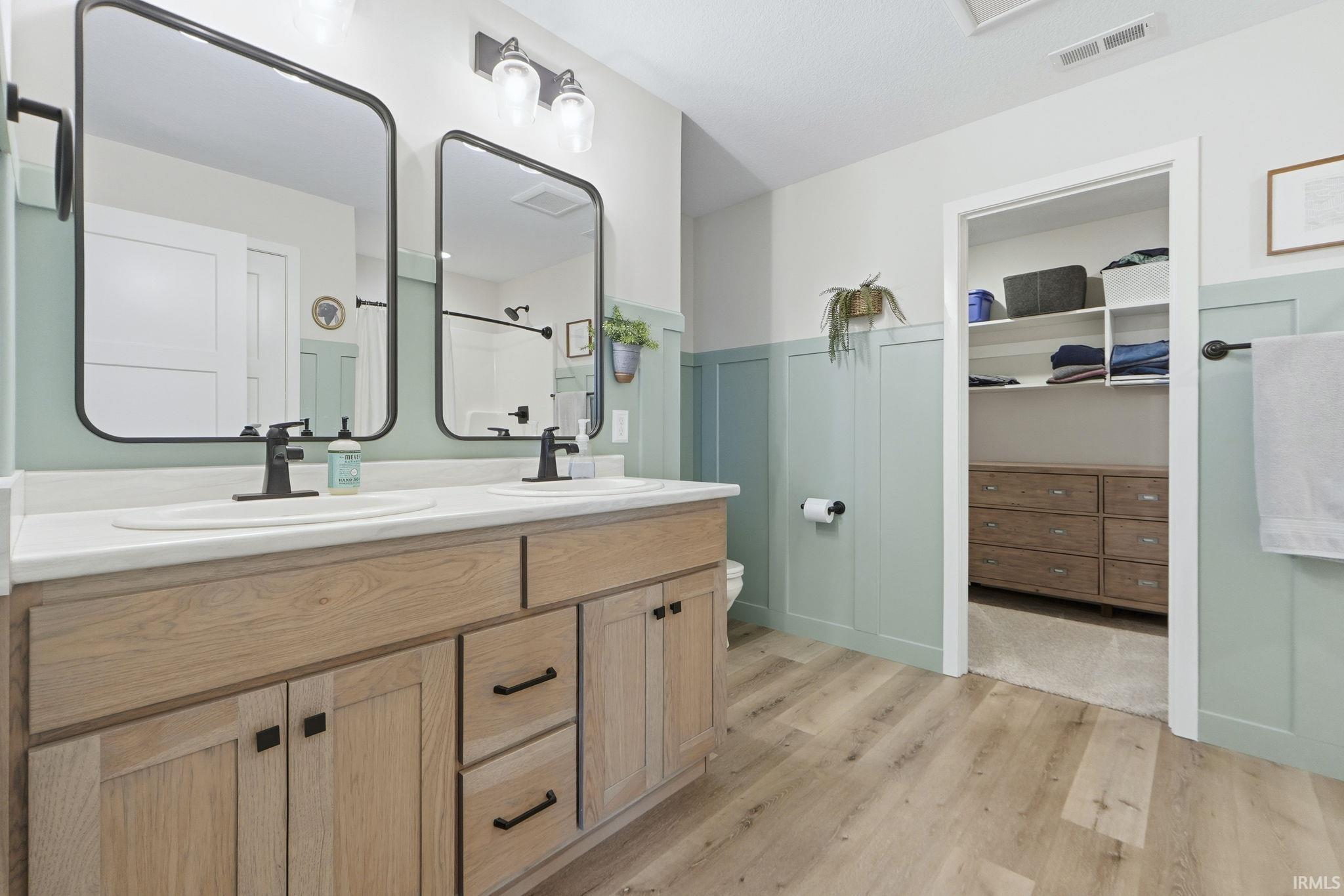 Bathroom featuring double vanity, a spacious closet, light wood-style flooring, and a shower