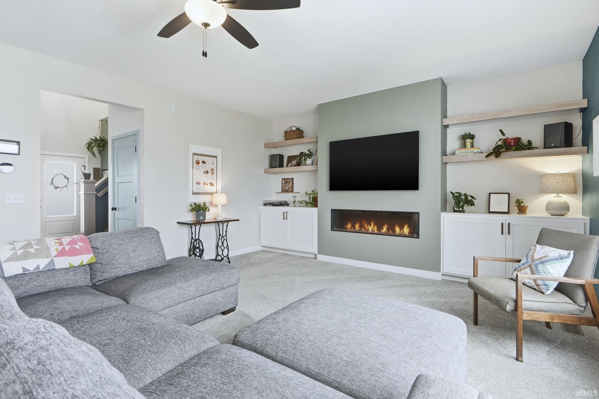 Carpeted living room featuring a ceiling fan and a glass covered fireplace
