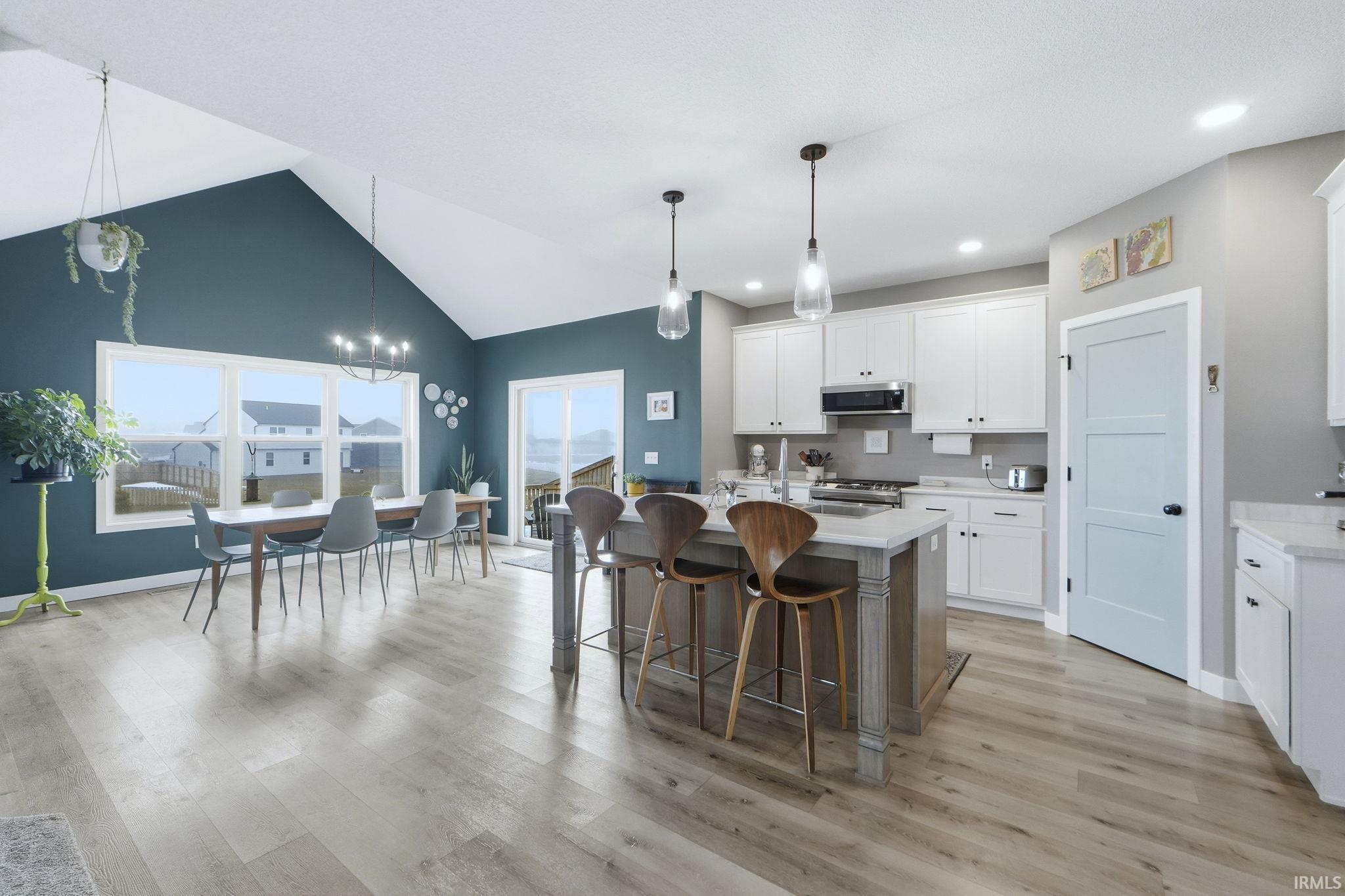 Kitchen with a kitchen island with sink, a breakfast bar, two tone cabinetry, vaulted ceiling, and light wood-style flooring