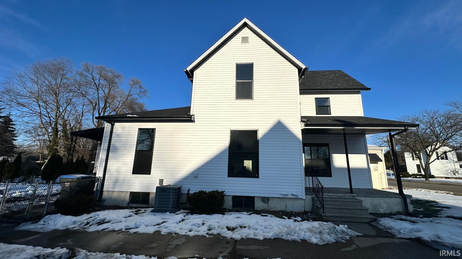 View of snowy exterior with a shingled roof and covered porch