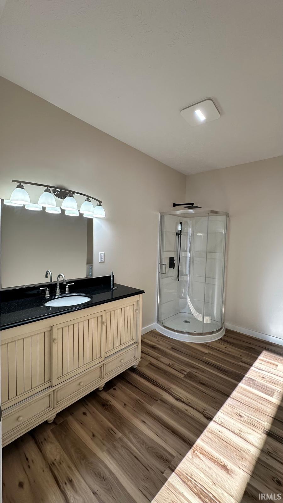 Full bath with vanity, a shower stall, and dark wood-style flooring