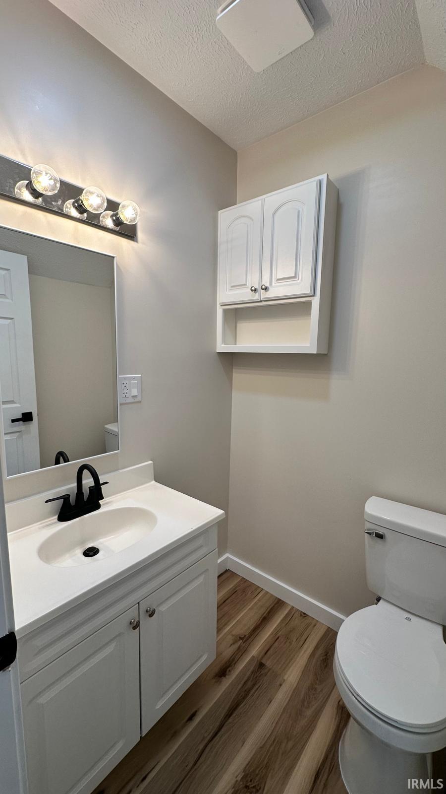 Half bathroom with vanity, a textured ceiling, and dark wood-style flooring