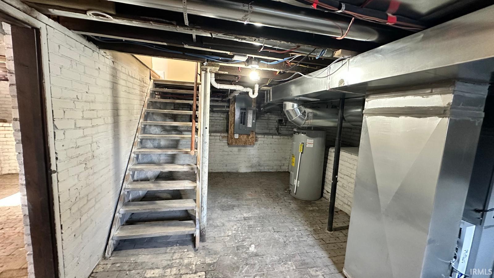 Unfinished below grade area with heating unit, water heater, and electric panel