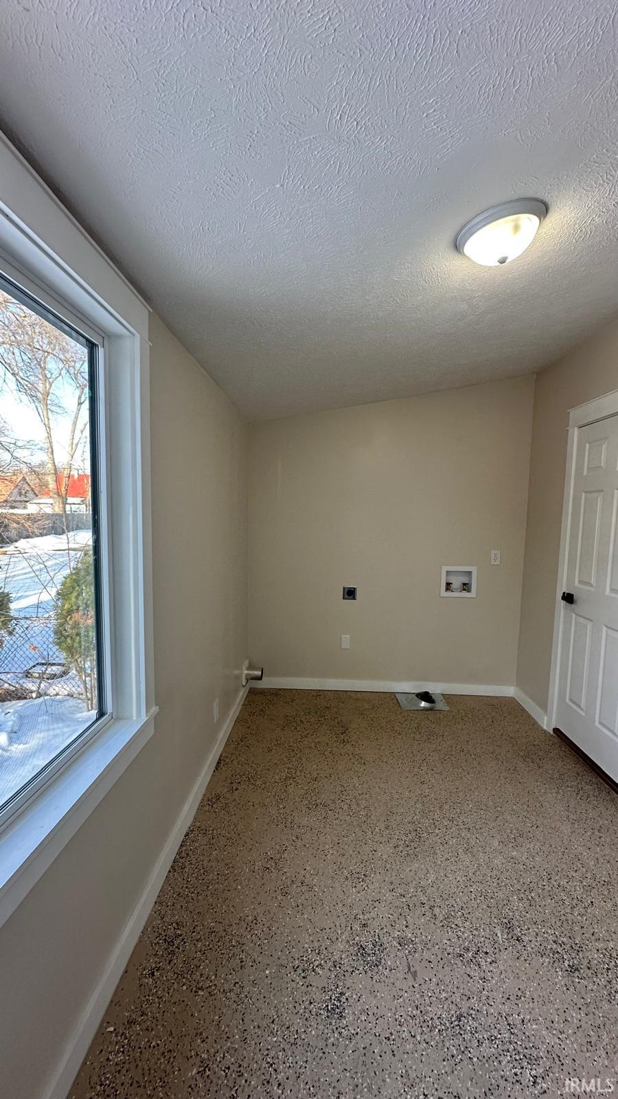 Laundry area with a textured ceiling, speckle patterned floor, and hookup for a washing machine