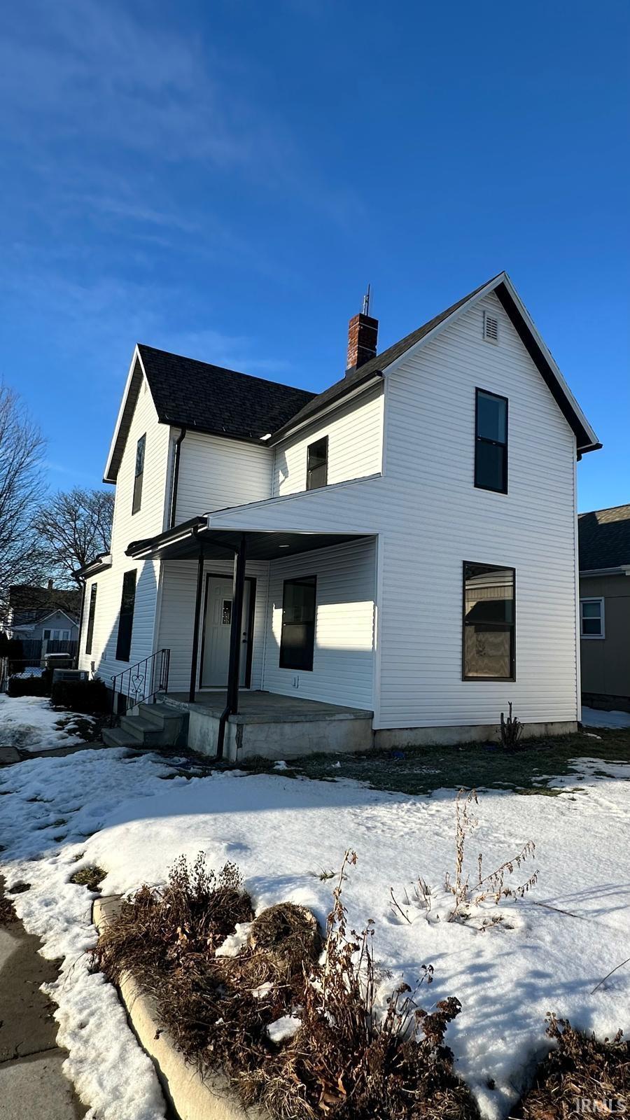 Snow covered rear of property with a chimney and a porch
