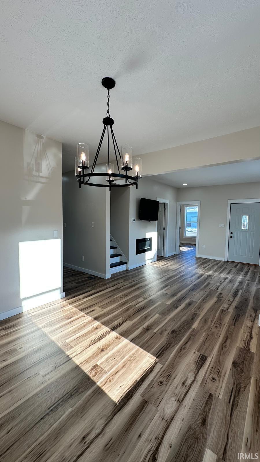 Unfurnished living room featuring suspended lighting and wood finished floors