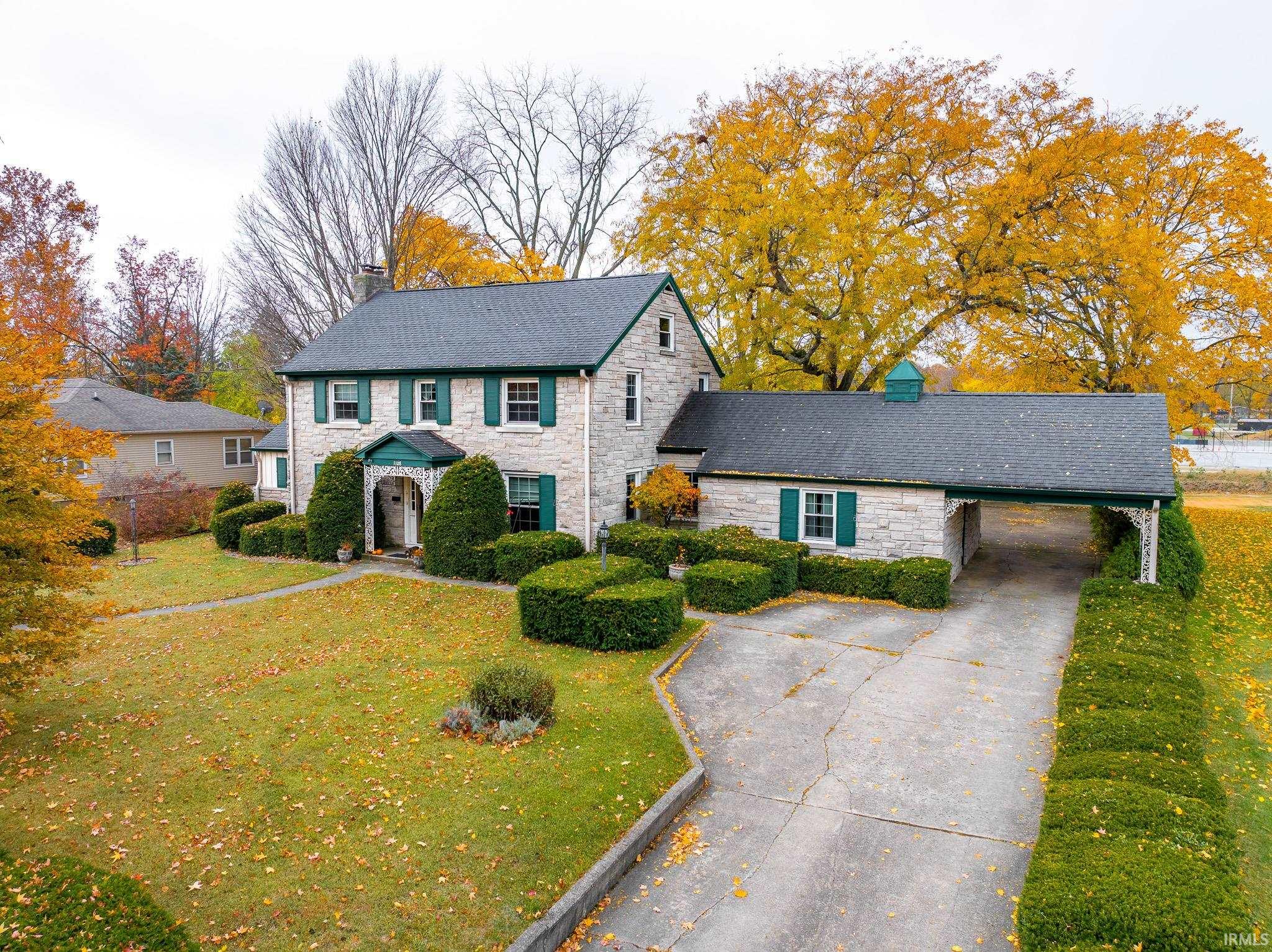 View of front of property with a chimney, driveway, stone siding, a front lawn, and a carport