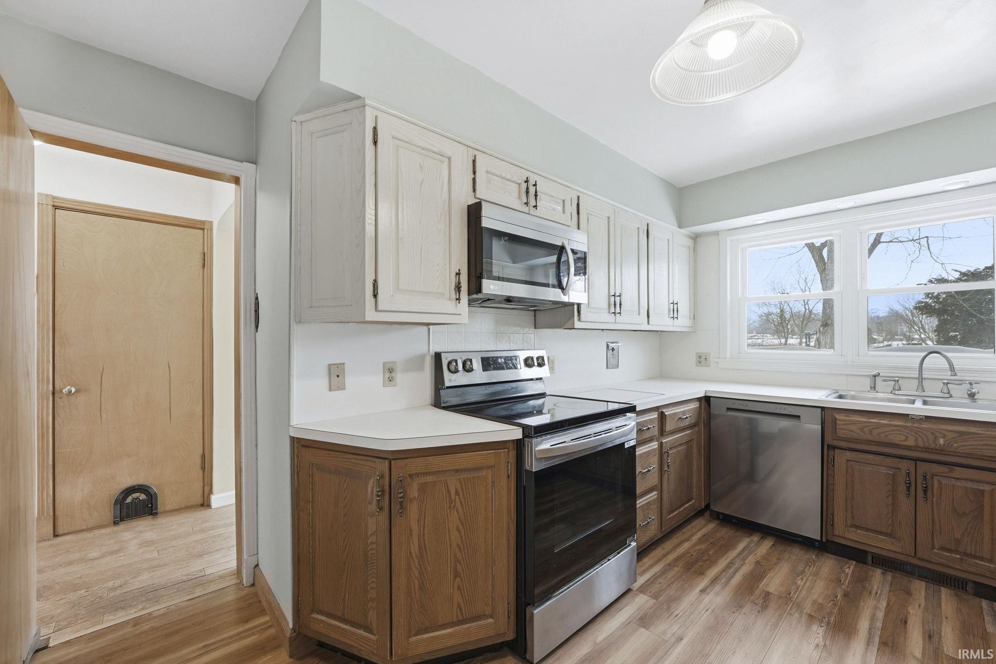 Kitchen featuring stainless steel appliances, light countertops, light wood finished floors, two tone cabinets, and decorative backsplash