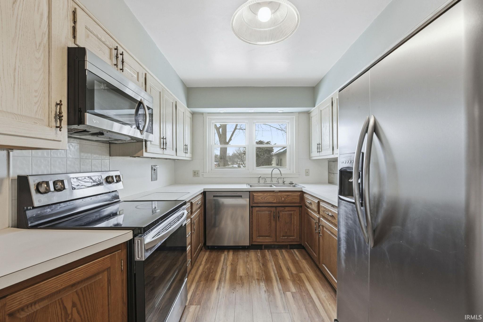 Two tone kitchen featuring stainless steel appliances, light countertops, dark wood-type flooring, two tone color scheme, and backsplash