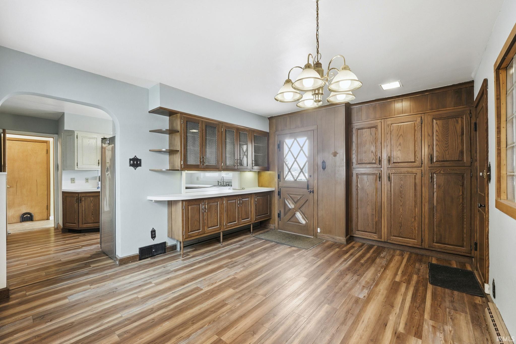 Kitchen with glass insert cabinets, arched walkways, light countertops, open shelves, and light wood-style floors