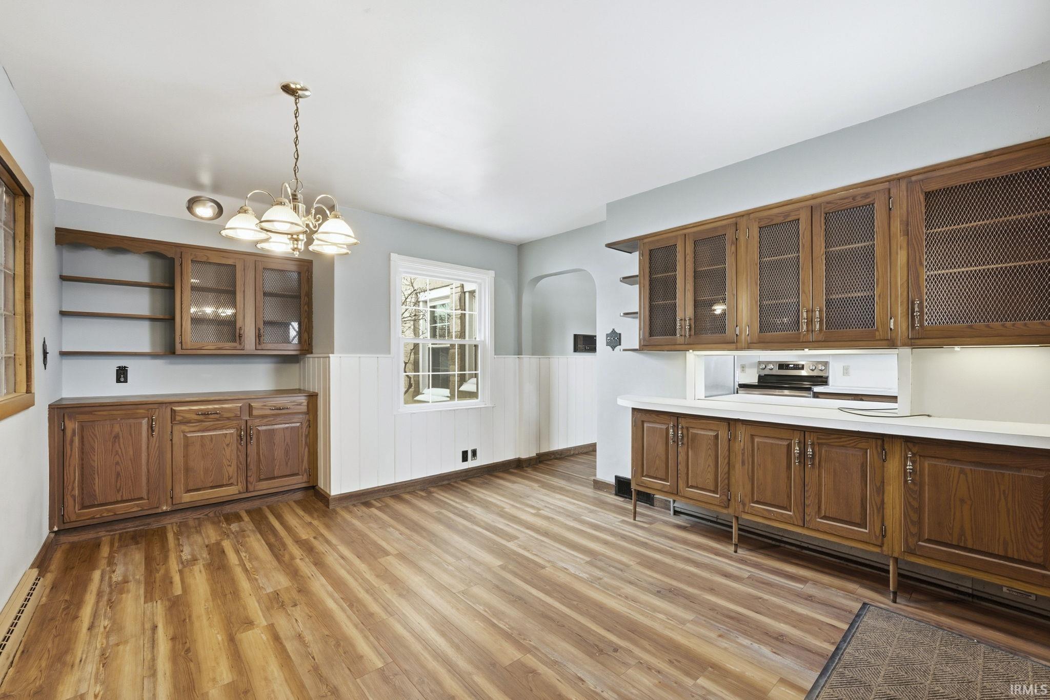 Kitchen with open shelves, glass insert cabinets, wainscoting, wood finish cabinets, and arched walkways