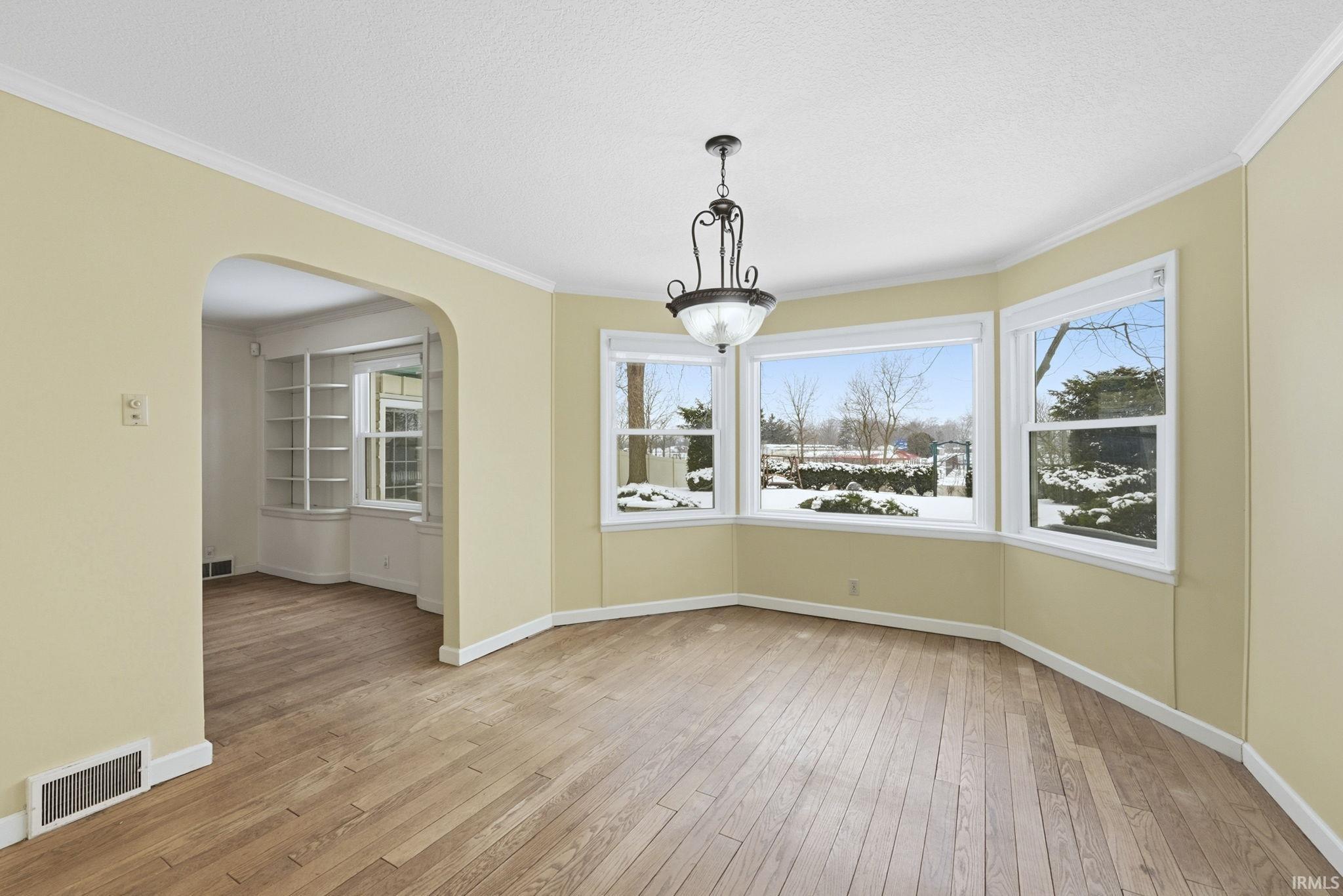 Unfurnished dining area featuring light wood-type flooring, plenty of natural light, arched walkways, crown molding, and a textured ceiling