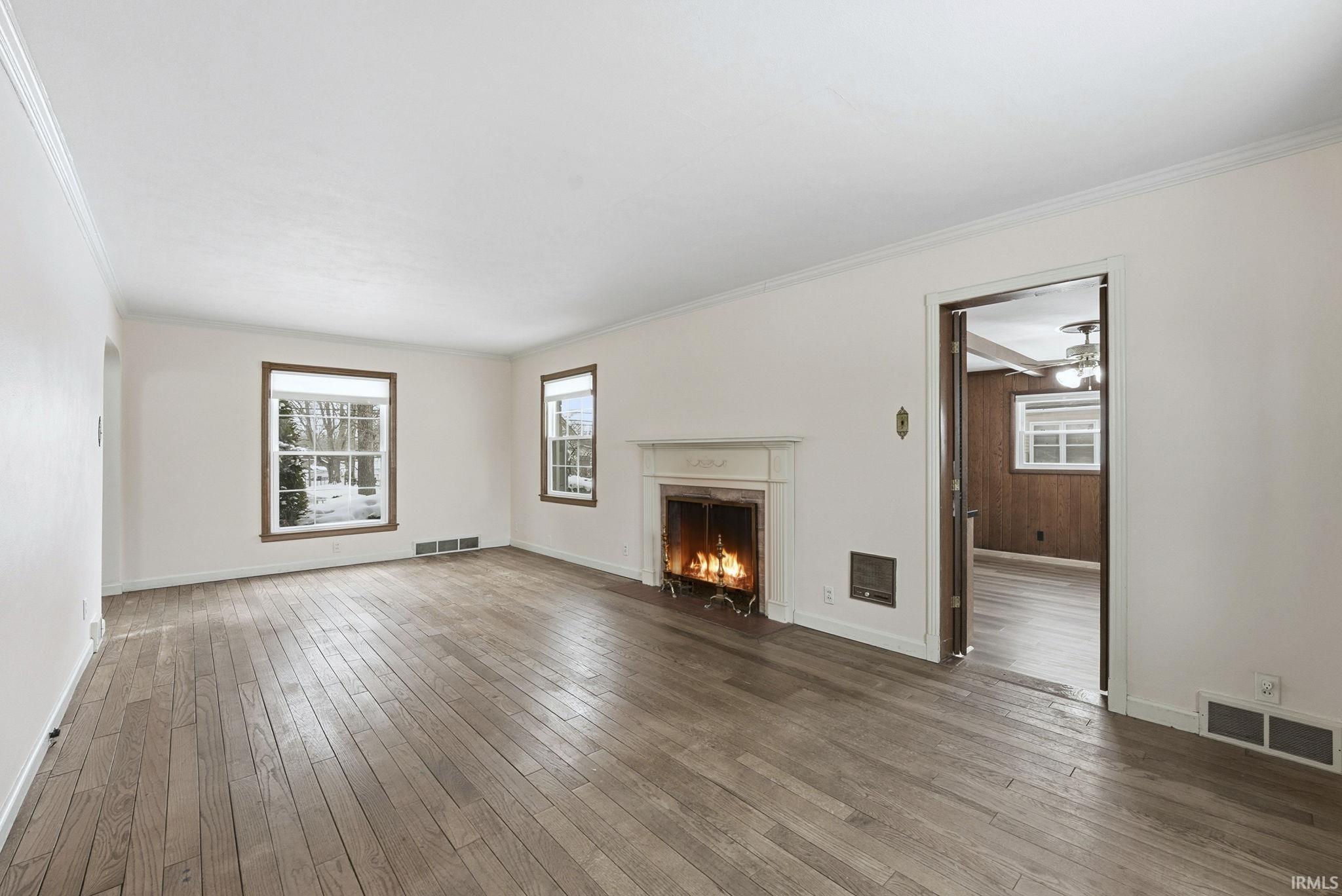 Unfurnished living room featuring a fireplace, hardwood / wood-style floors, crown molding, and arched walkways