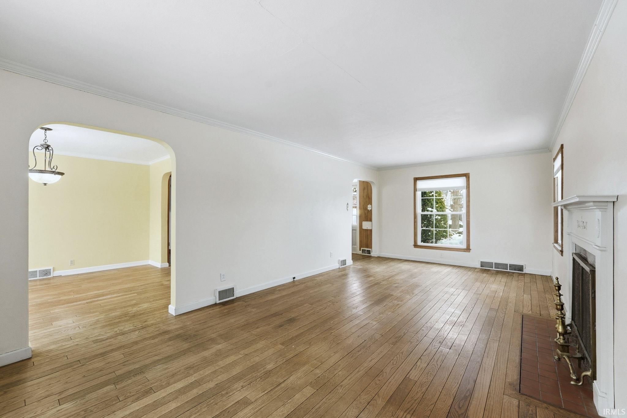 Unfurnished living room featuring arched walkways, light wood-type flooring, crown molding, and a fireplace