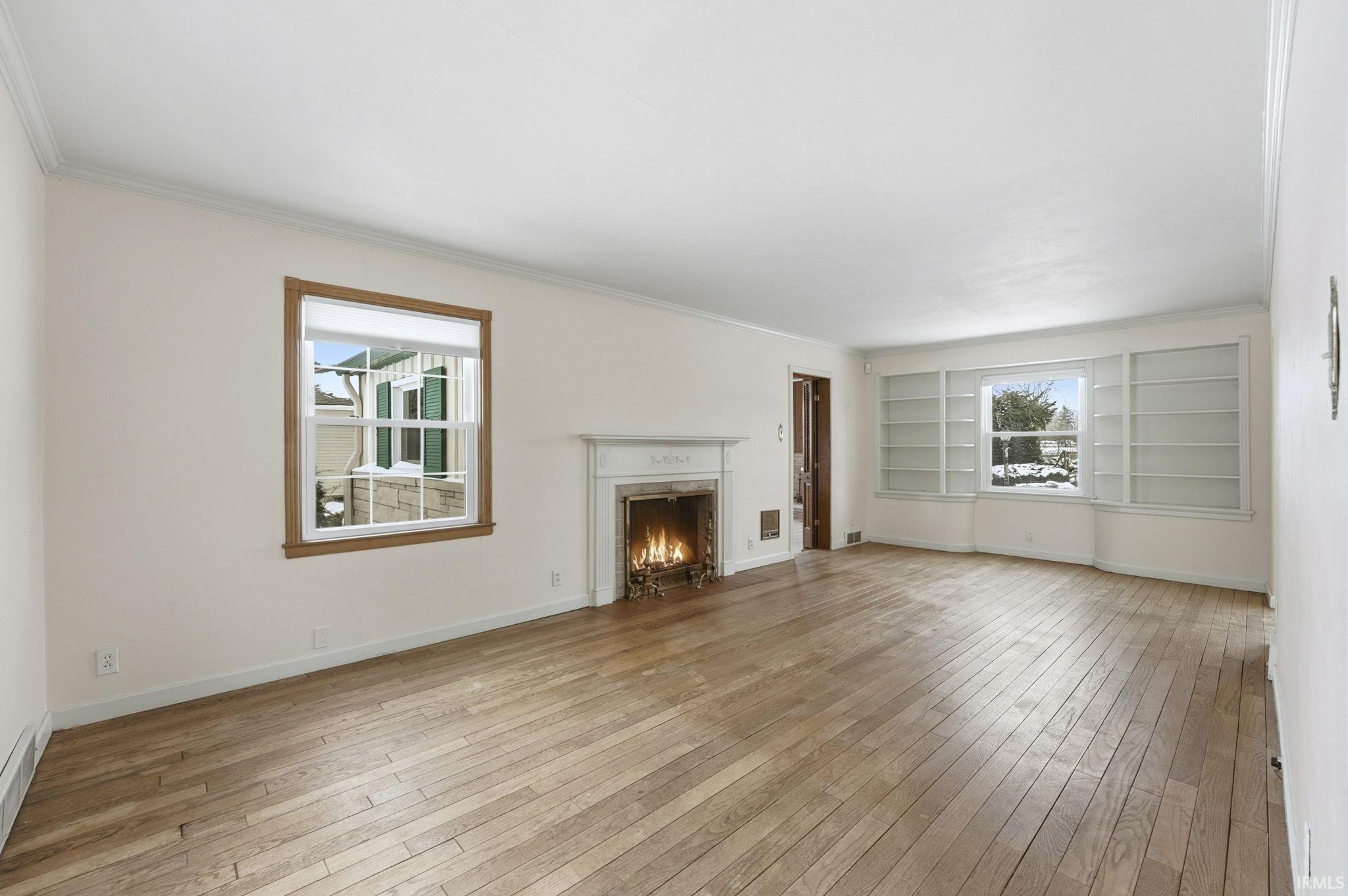 Unfurnished living room with crown molding, a high end fireplace, built in shelves, light wood-type flooring, and healthy amount of natural light