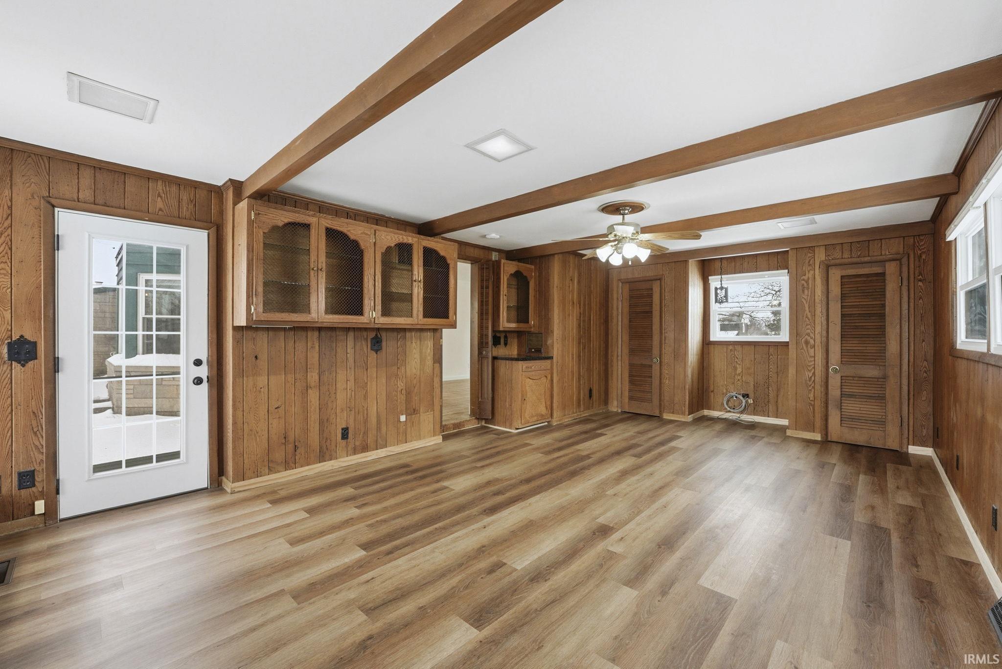 Unfurnished living room with wood walls, ceiling fan, beamed ceiling, and light wood-type flooring