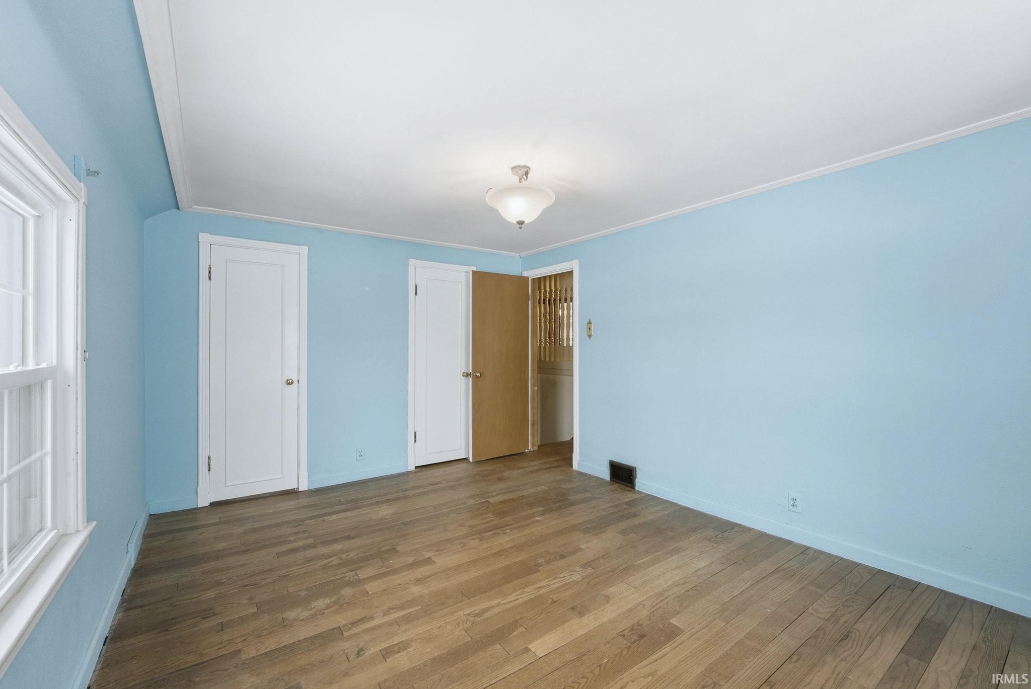 Unfurnished bedroom with wood-type flooring and ornamental molding
