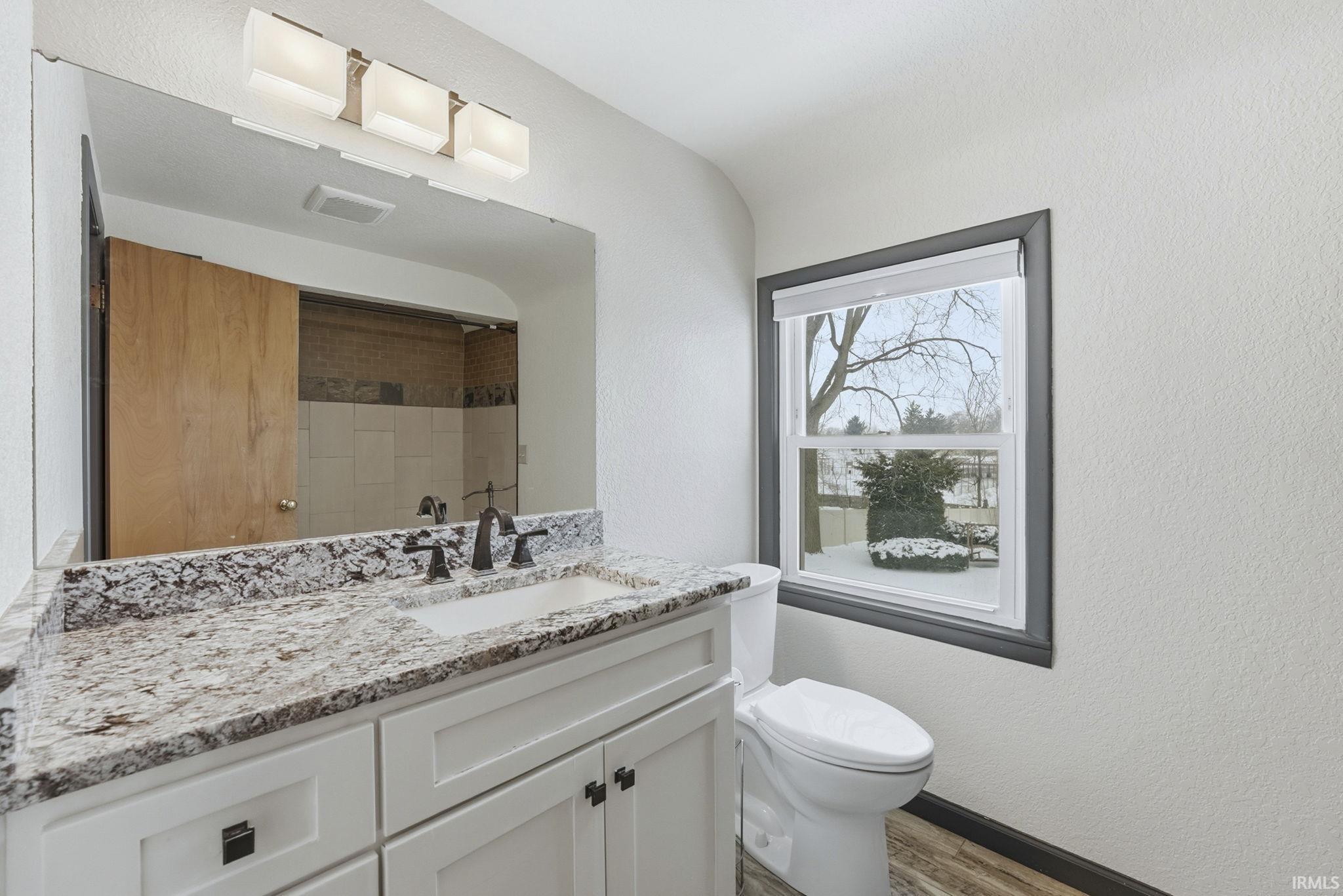 Full bath featuring a textured wall, vanity, tiled shower, and light wood-style floors