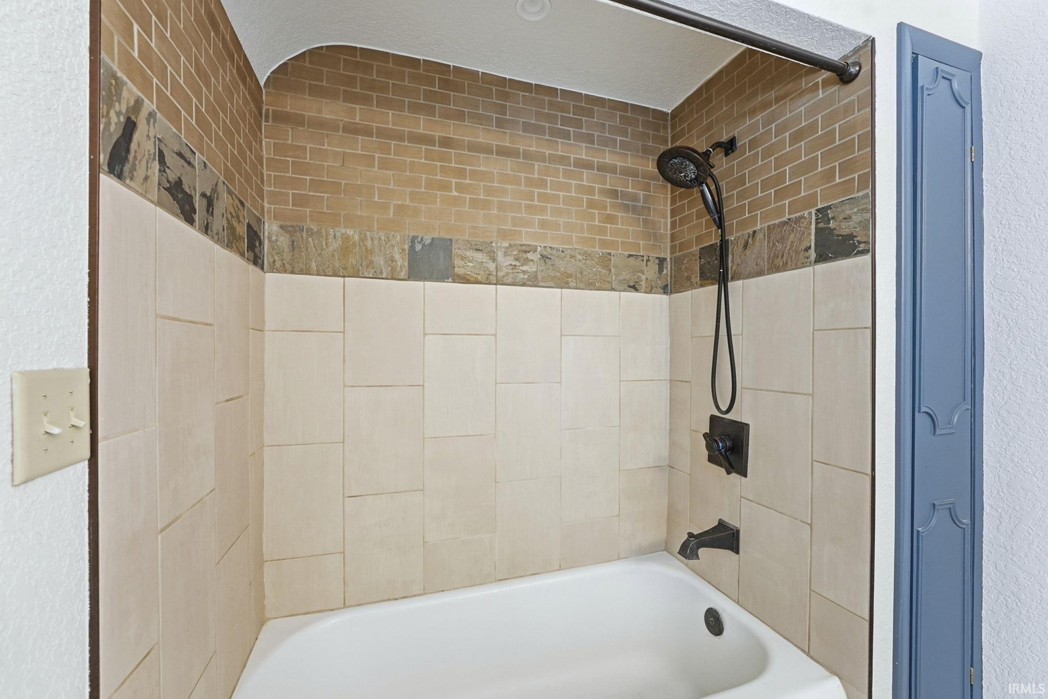 Full bath with bathtub / shower combination and a textured wall