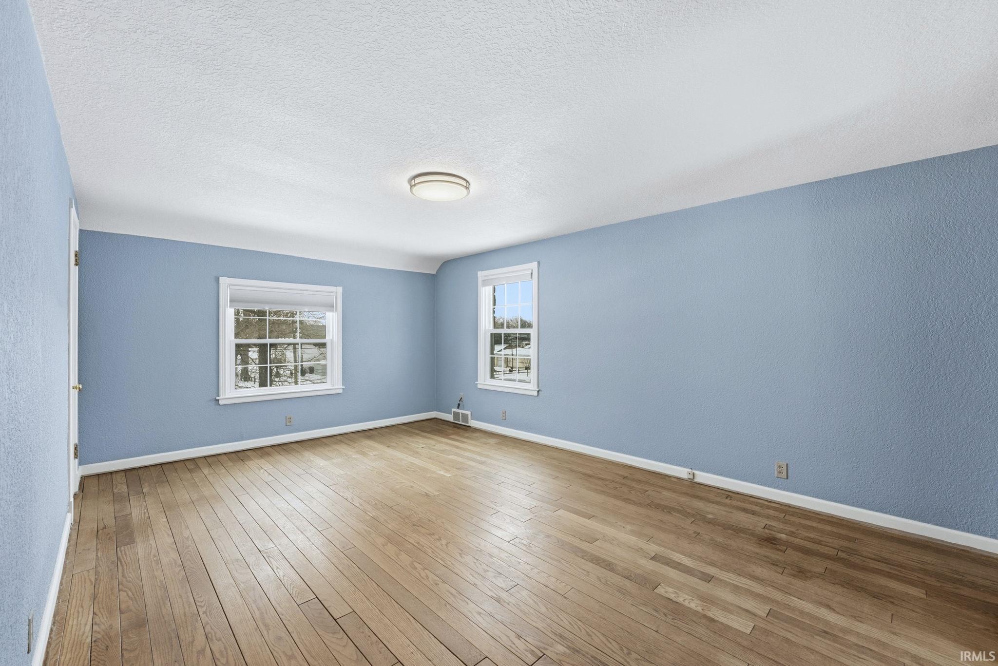 Spare room featuring a textured wall, light wood-type flooring, and a textured ceiling