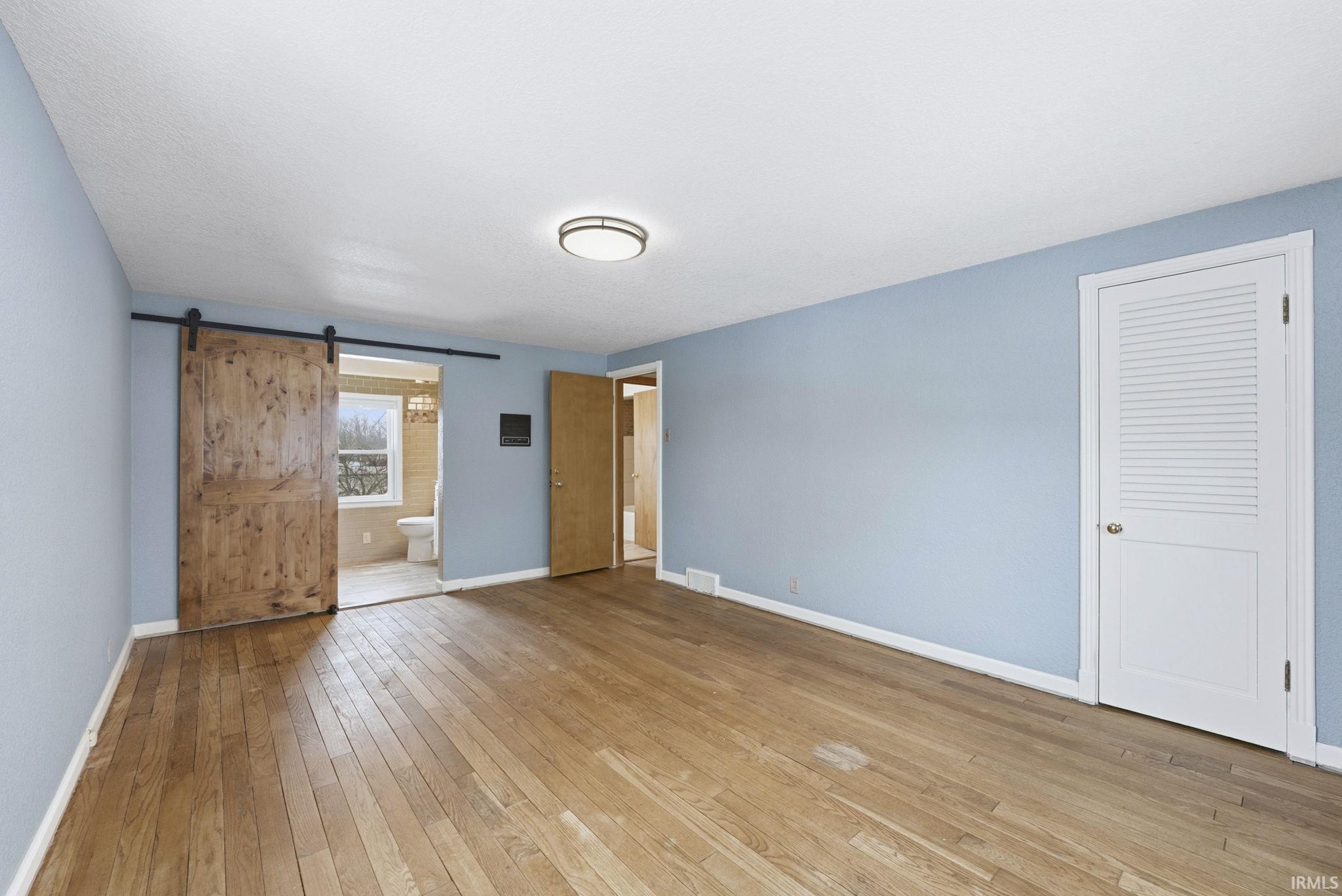 Unfurnished bedroom featuring a barn door, light wood finished floors, and connected bathroom