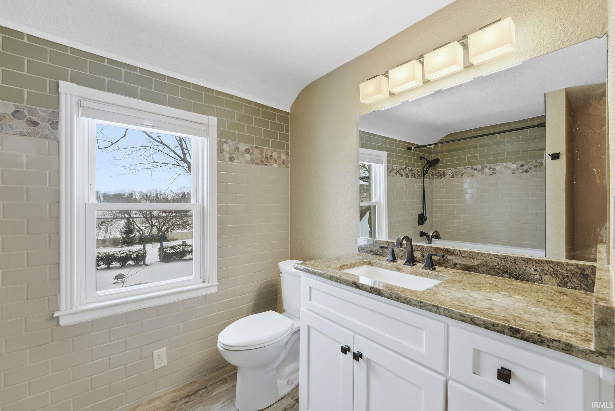 Full bath featuring vanity, tile walls, and light wood finished floors