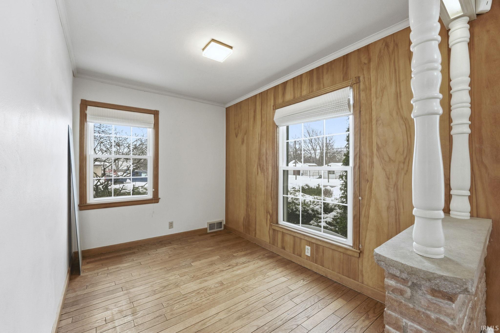 Unfurnished room with light wood-style floors, ornamental molding, and wooden walls