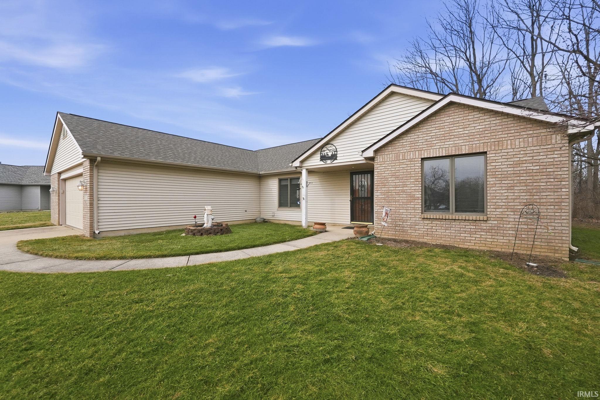 Ranch-style home featuring a front yard, driveway, an attached garage, roof with shingles, and brick siding