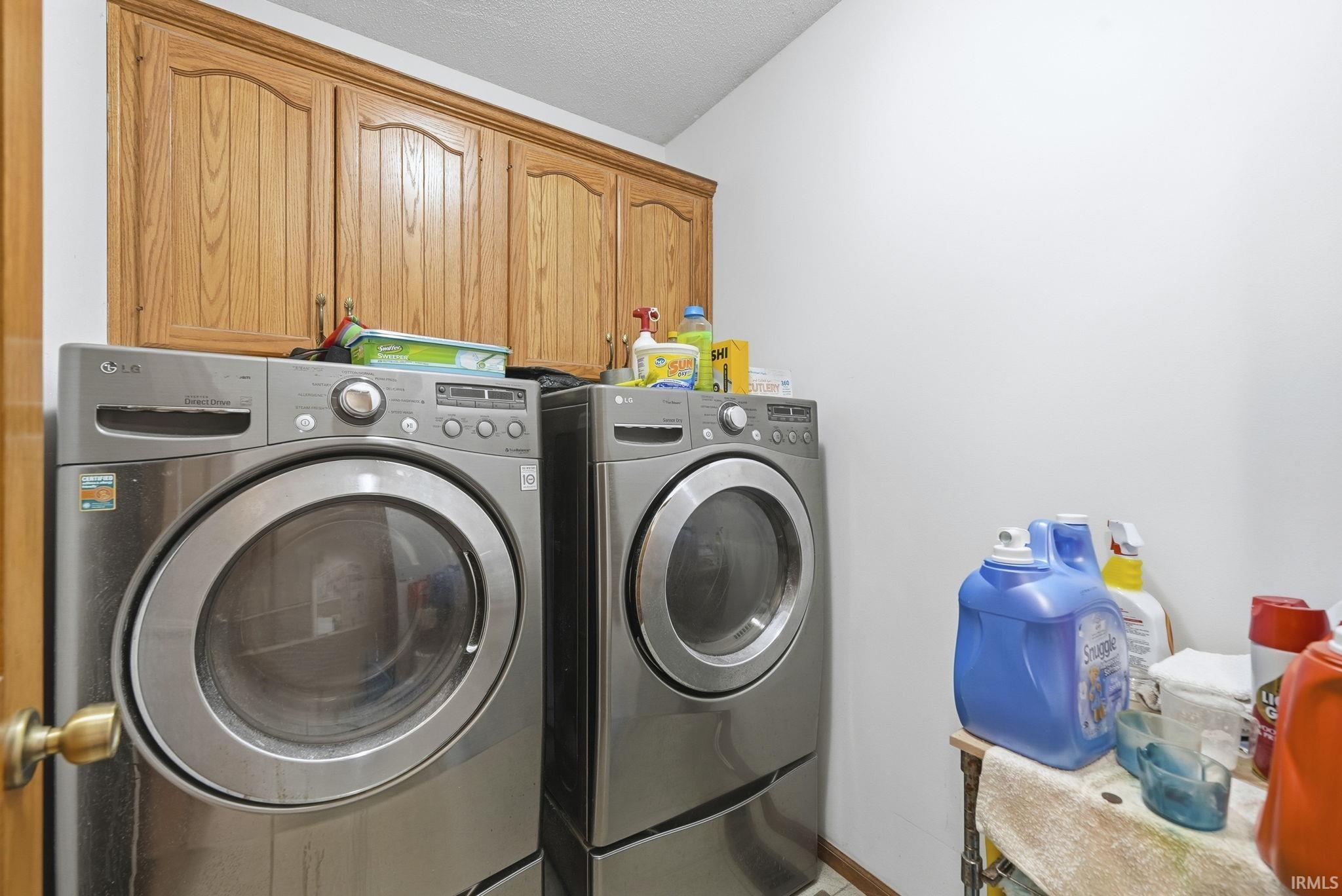 Laundry room featuring washing machine and dryer, a textured ceiling, and cabinet space