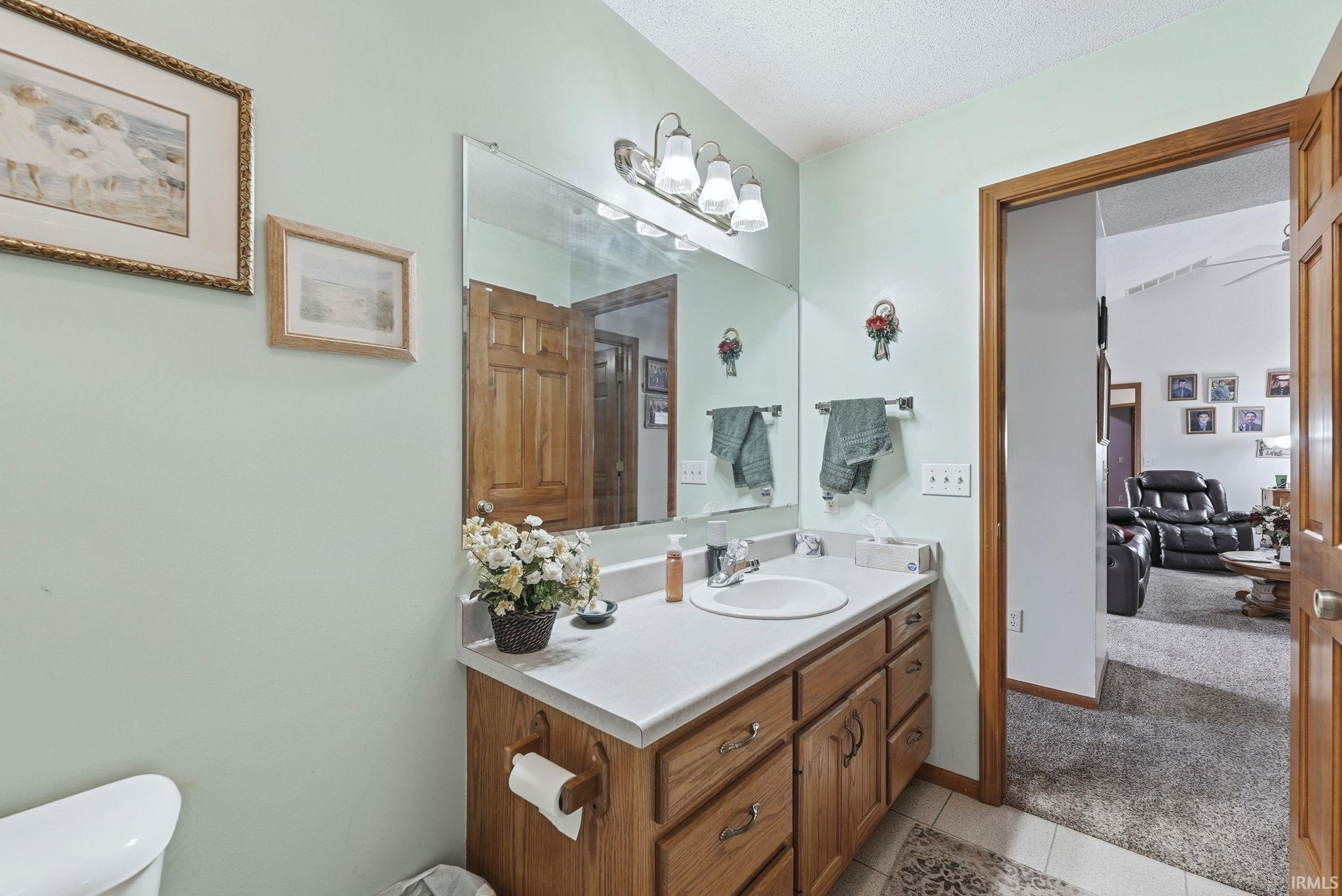 Bathroom featuring vanity, a textured ceiling, light colored carpet, and light tile patterned floors