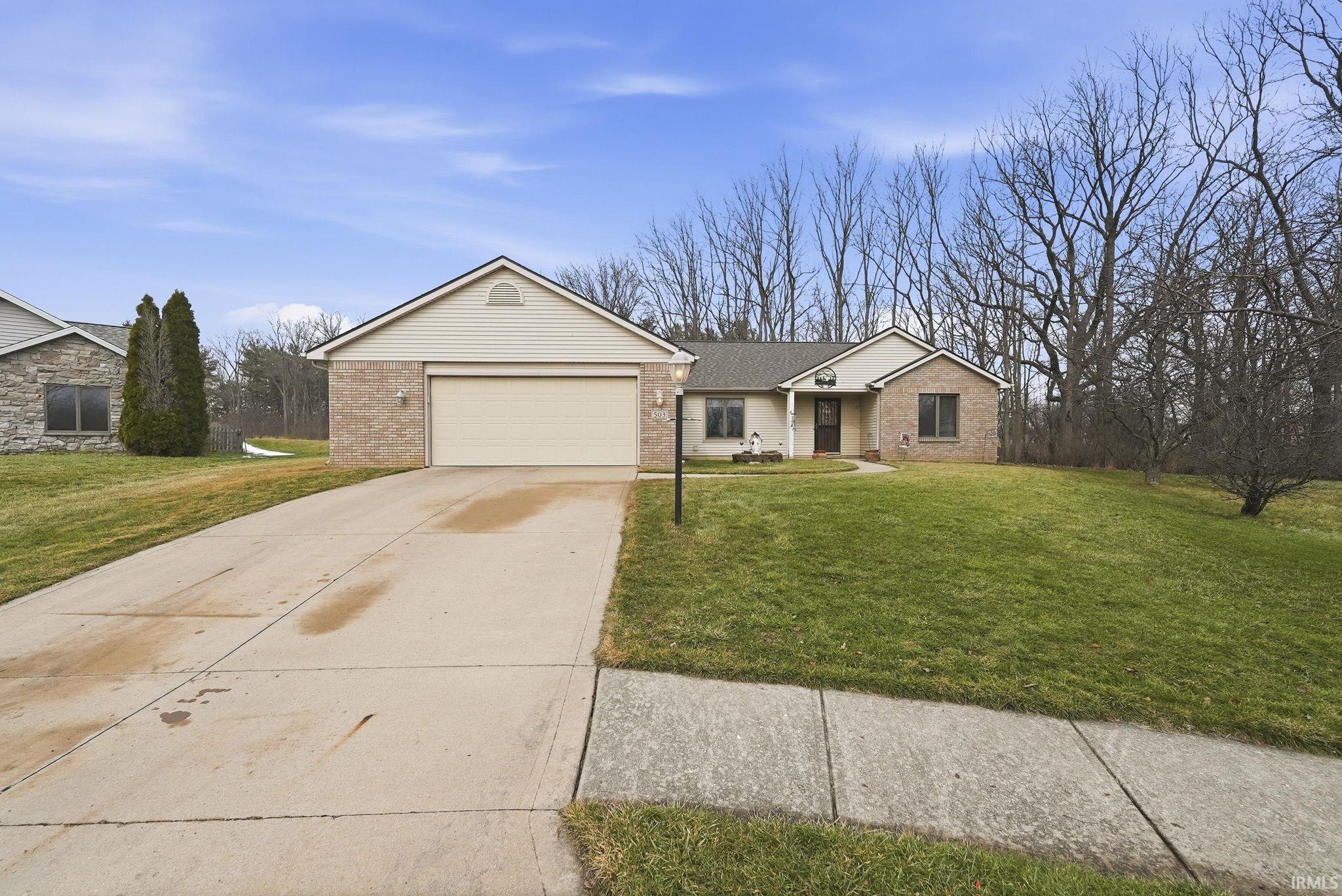 Single story home featuring a front yard, concrete driveway, brick siding, and a garage