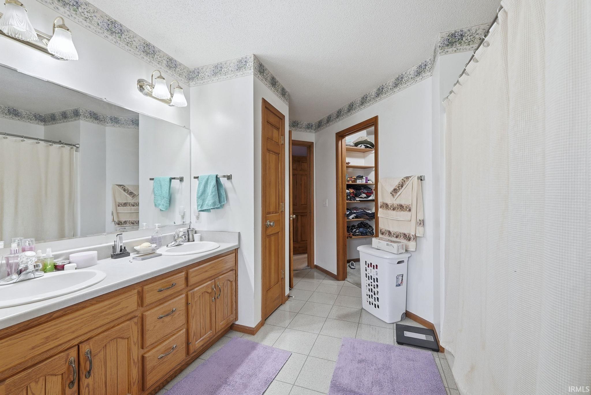 Full bath featuring curtained shower, double vanity, light tile patterned floors, and a walk in closet
