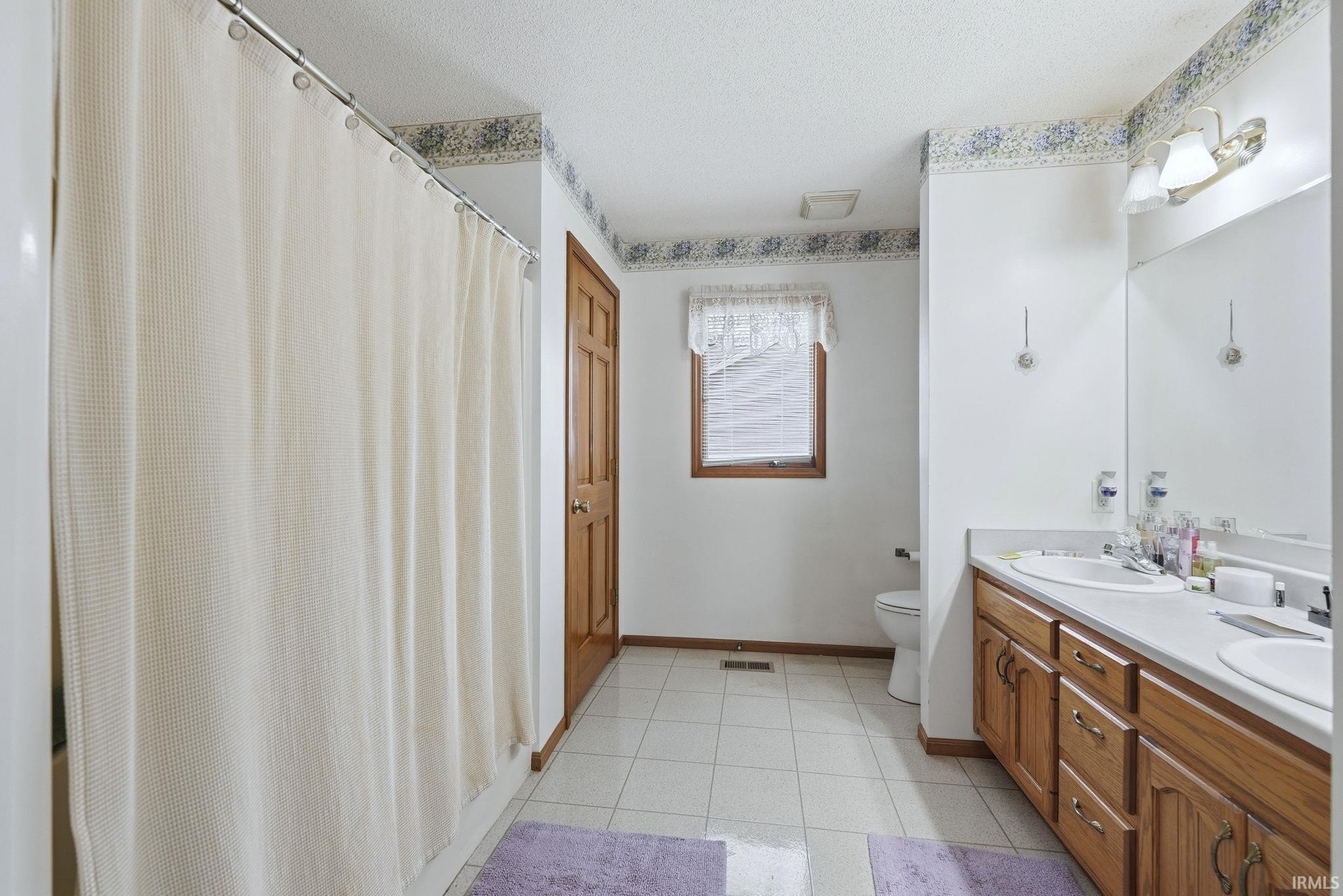 Full bathroom with a shower with shower curtain, double vanity, and a textured ceiling