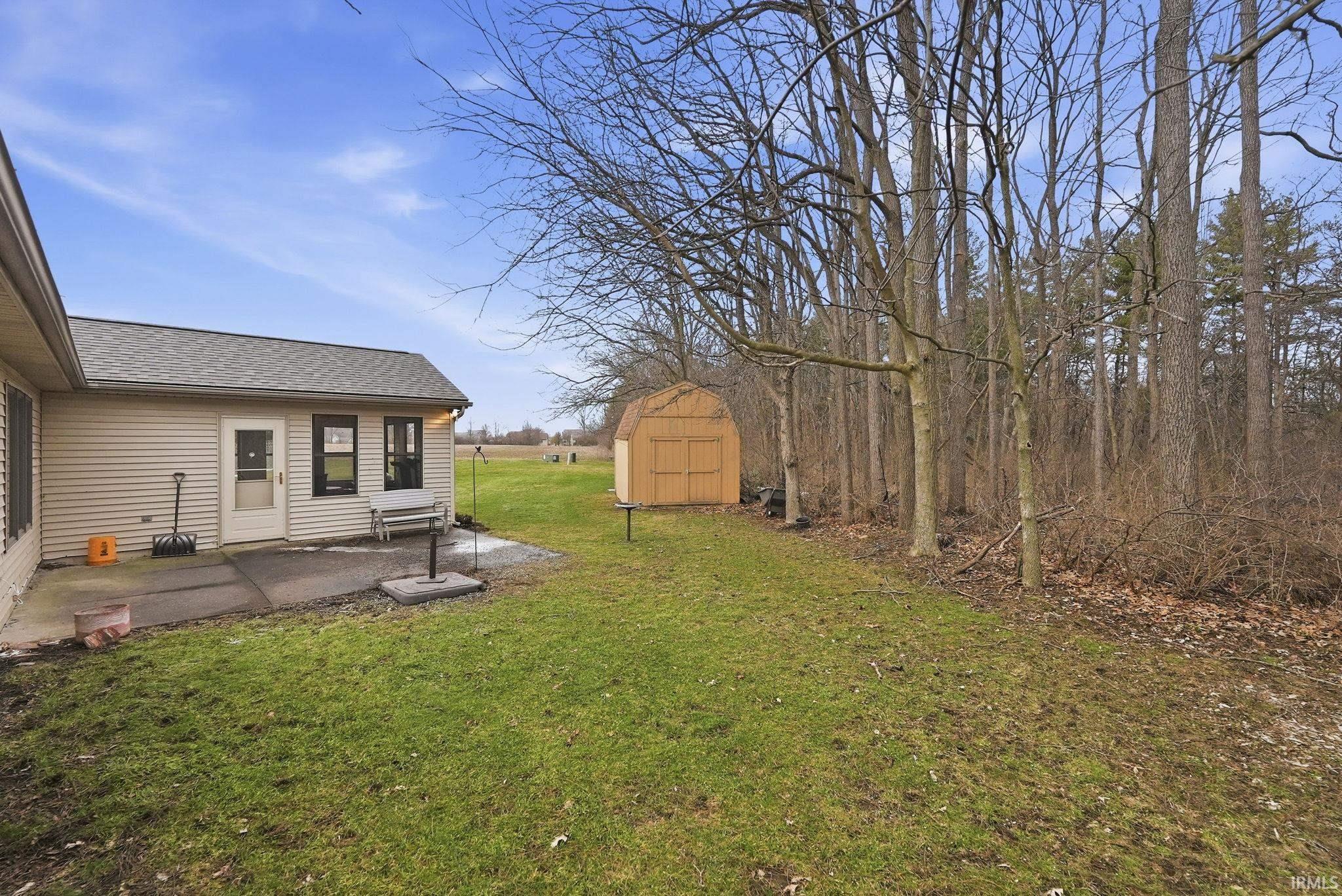 View of grassy yard featuring a patio and a storage unit
