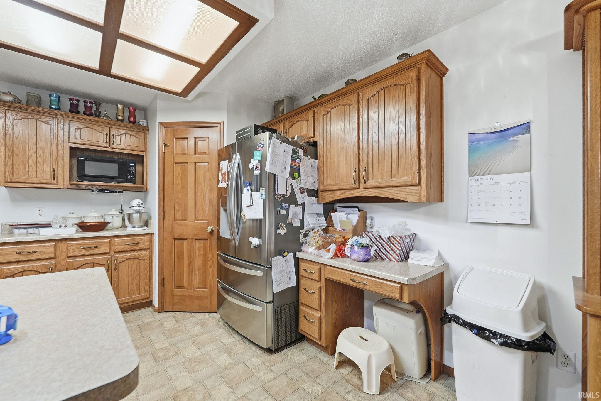Kitchen featuring light countertops, wood finish cabinets, stainless steel fridge with ice dispenser, and black microwave