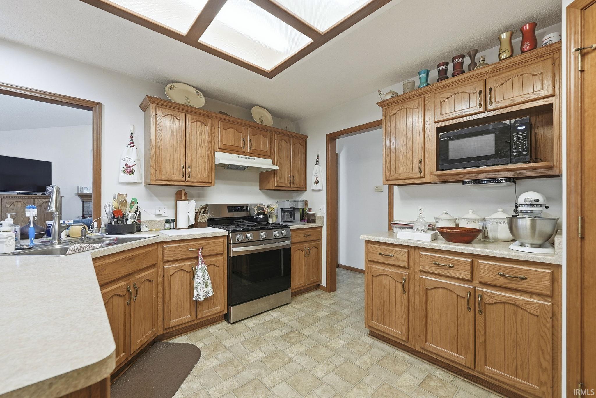 Kitchen featuring stainless steel gas range, light countertops, black microwave, and wood finish cabinets
