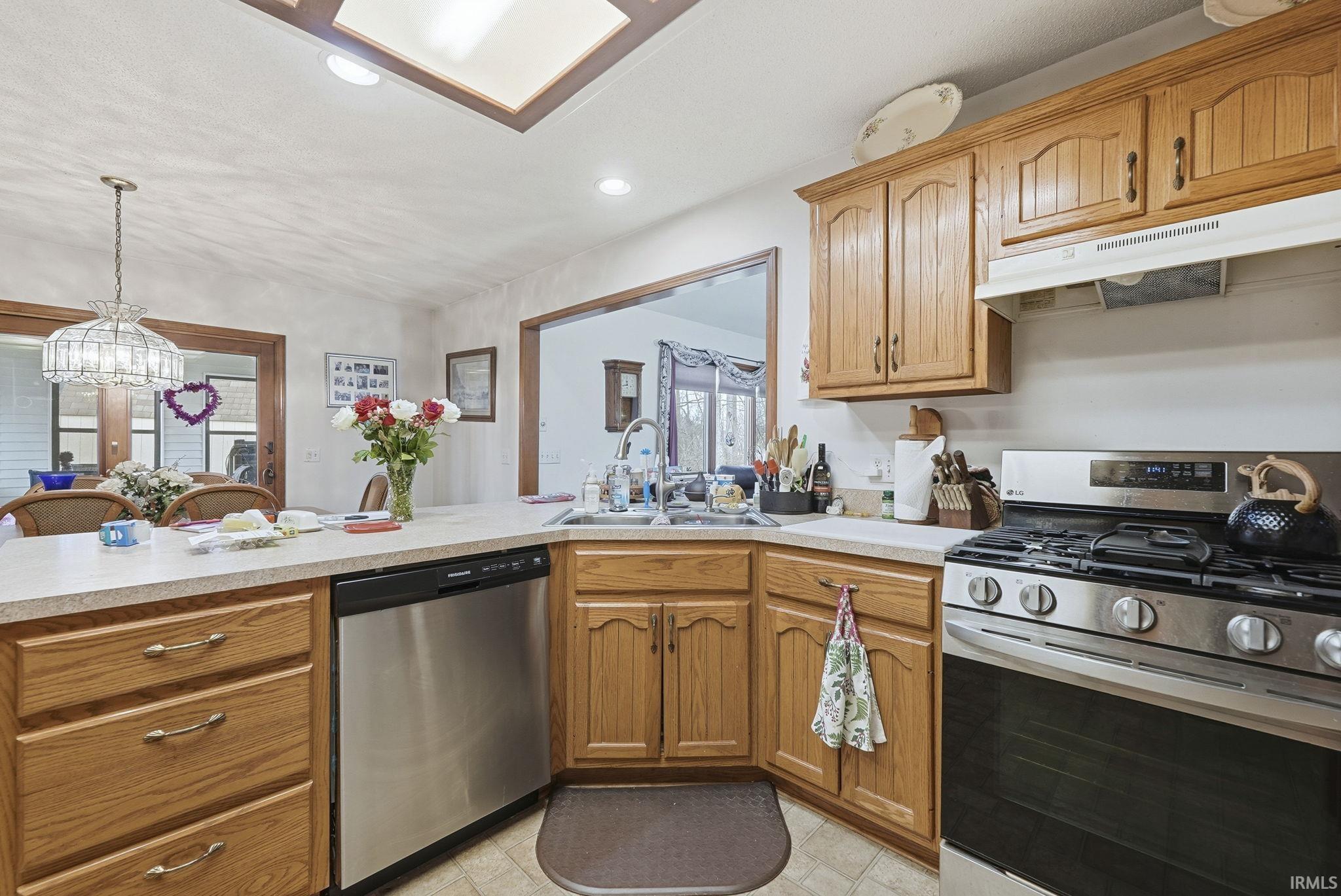 Kitchen featuring stainless steel appliances, light countertops, wood finish cabinets, vaulted ceiling, and a peninsula