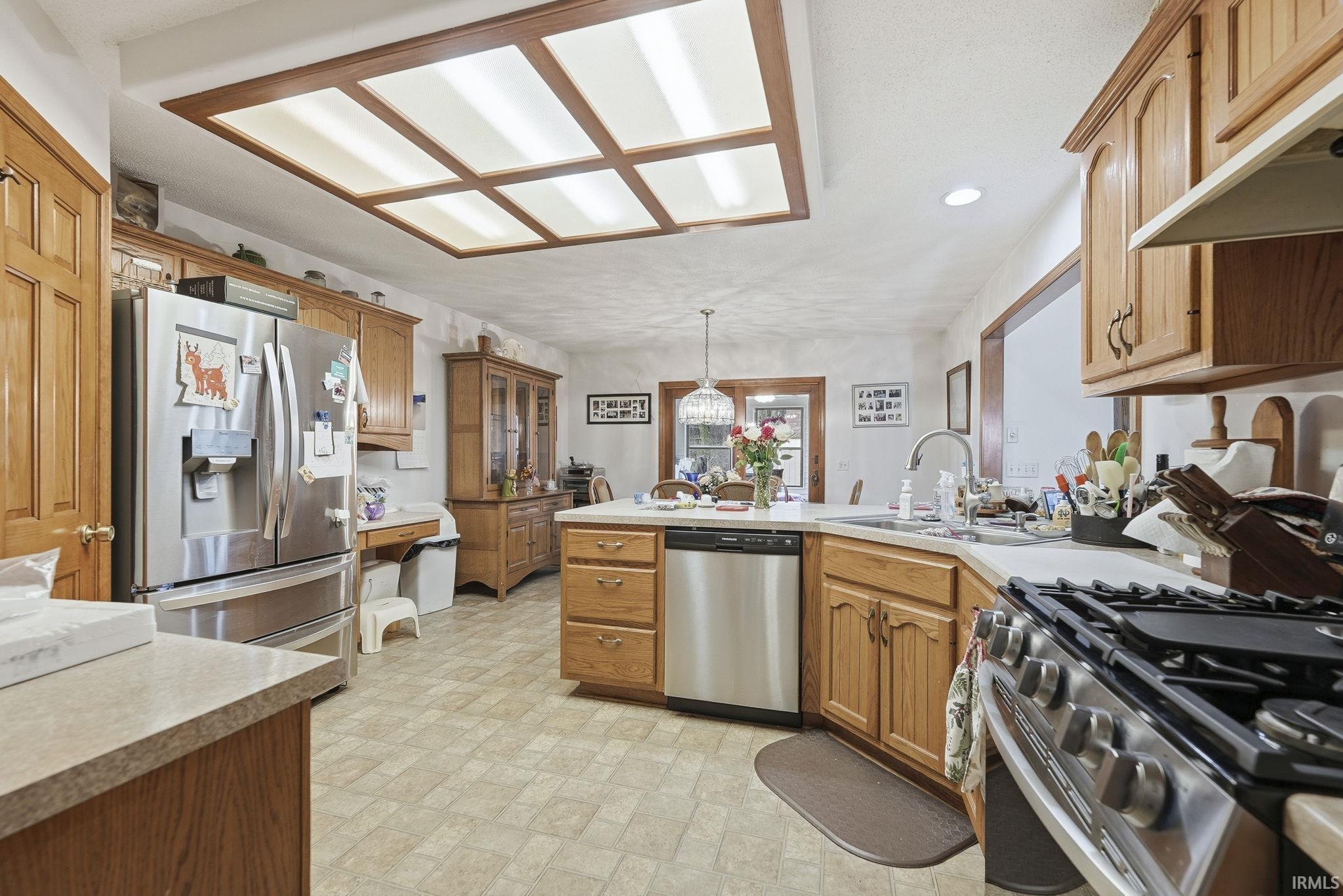 Kitchen with a peninsula, stainless steel appliances, wood finish cabinetry, light countertops, and hanging lights