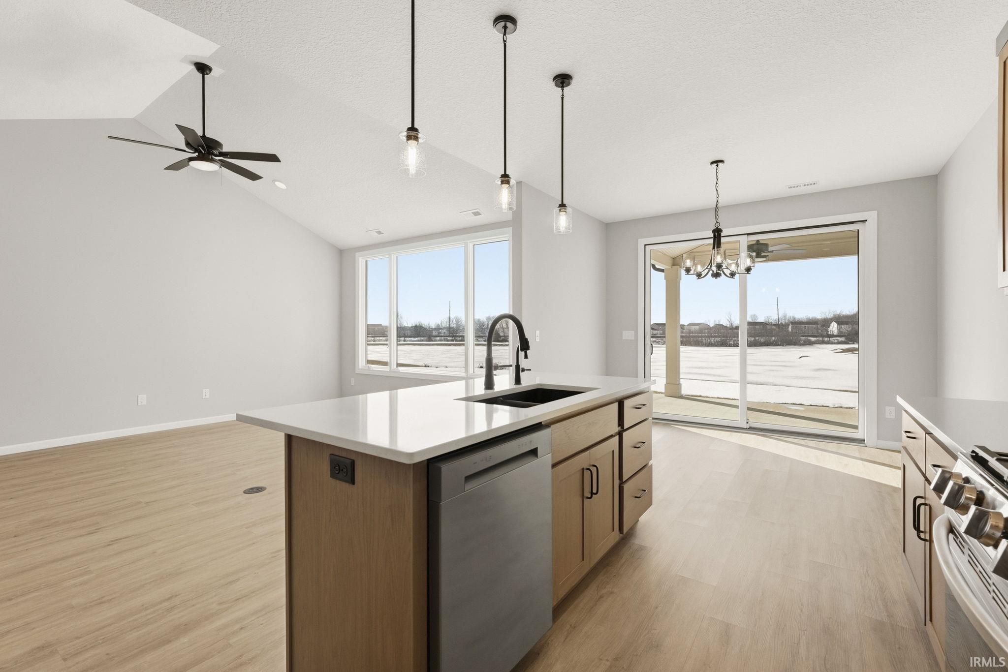 Kitchen with suspended lighting, stainless steel appliances, a kitchen island with sink, lofted ceiling, and light wood finished floors