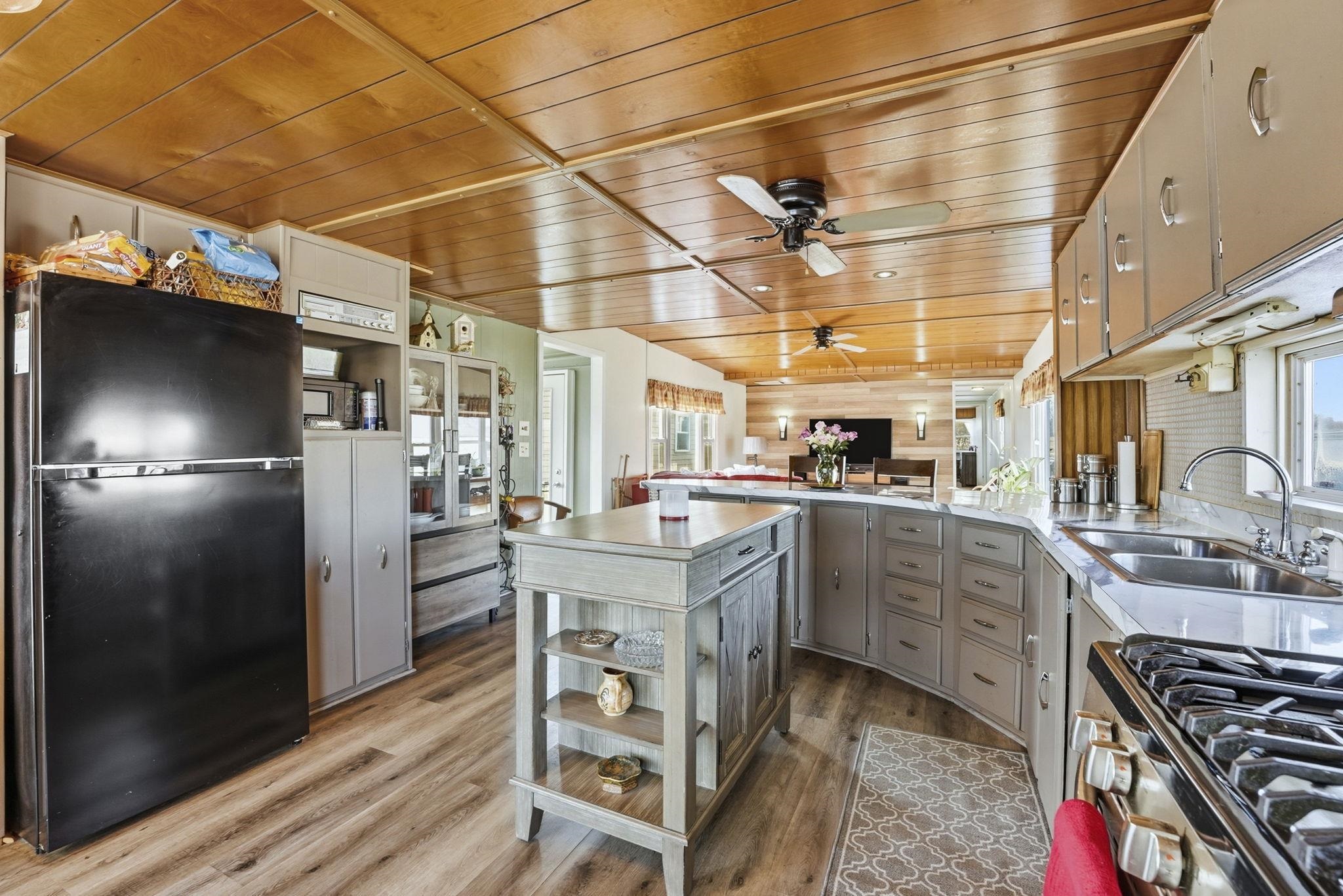 Kitchen featuring freestanding refrigerator, a peninsula, wood ceiling, dark wood-style floors, and a ceiling fan