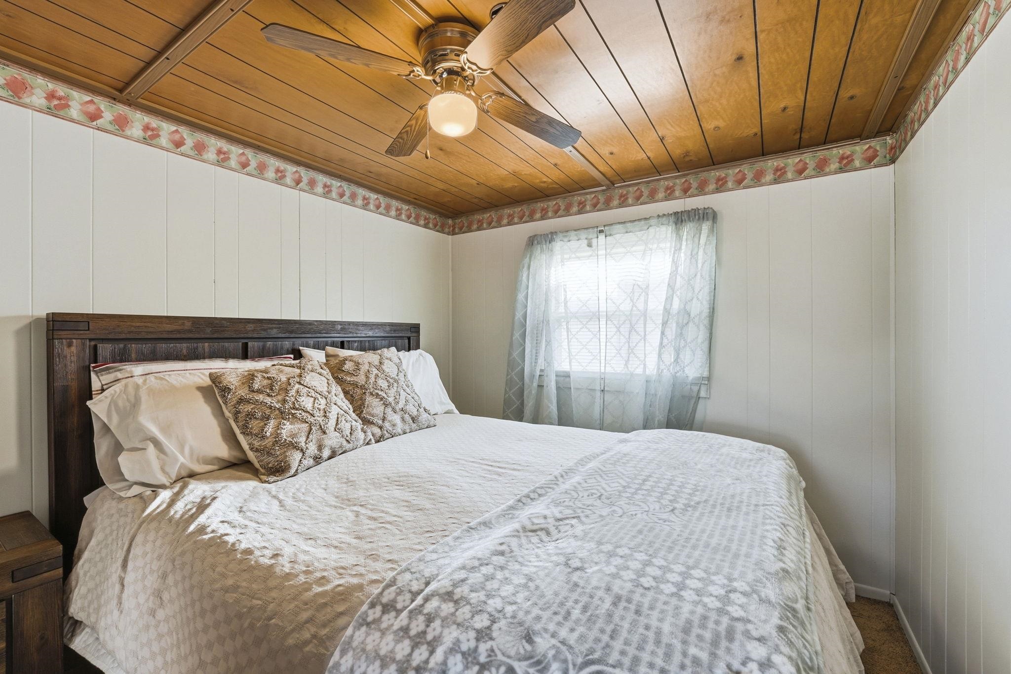 Carpeted bedroom with wood ceiling, a ceiling fan, and wood walls