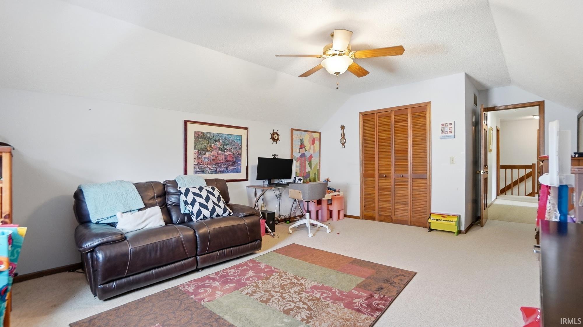 Carpeted living area with a ceiling fan and vaulted ceiling