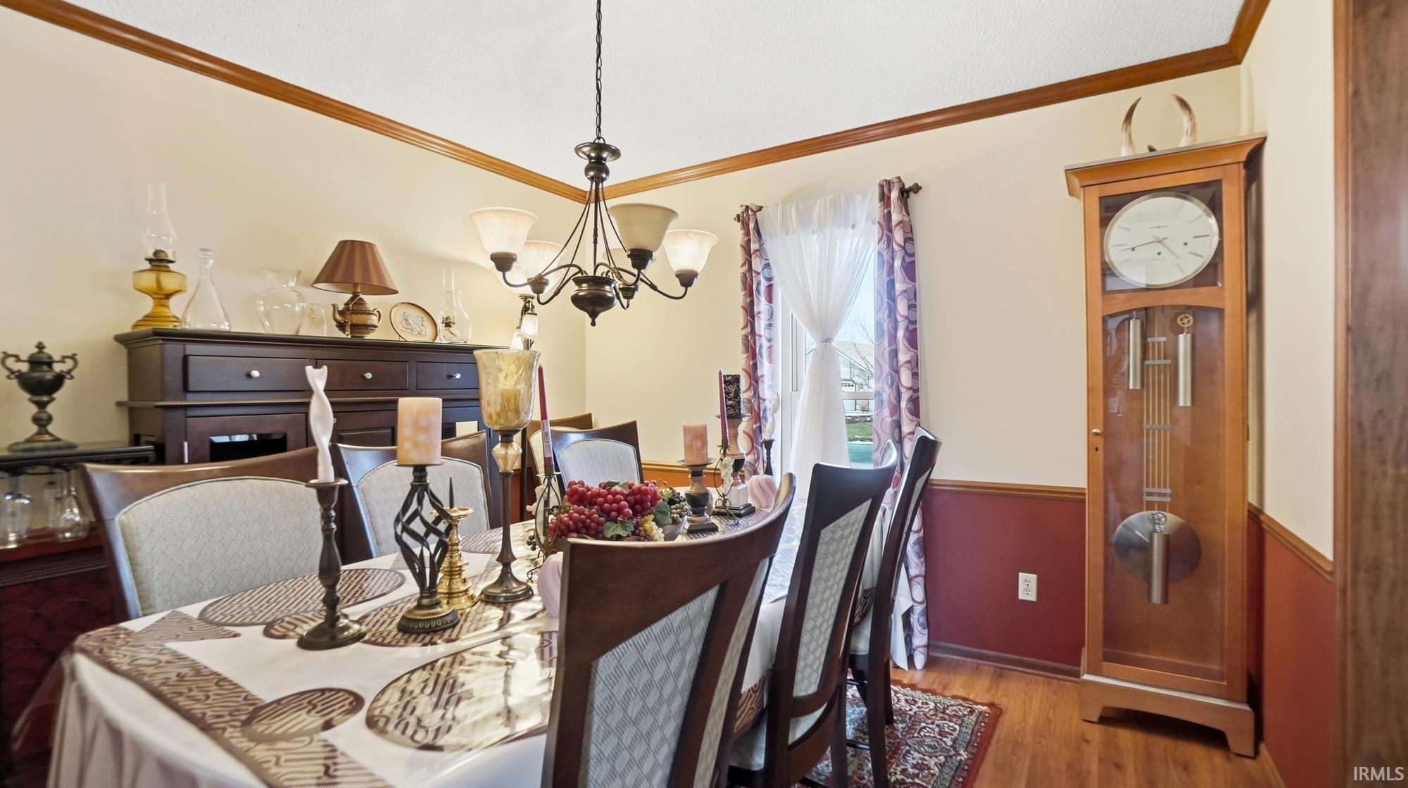 Dining space featuring hanging lights, wood finished floors, crown molding, and wainscoting