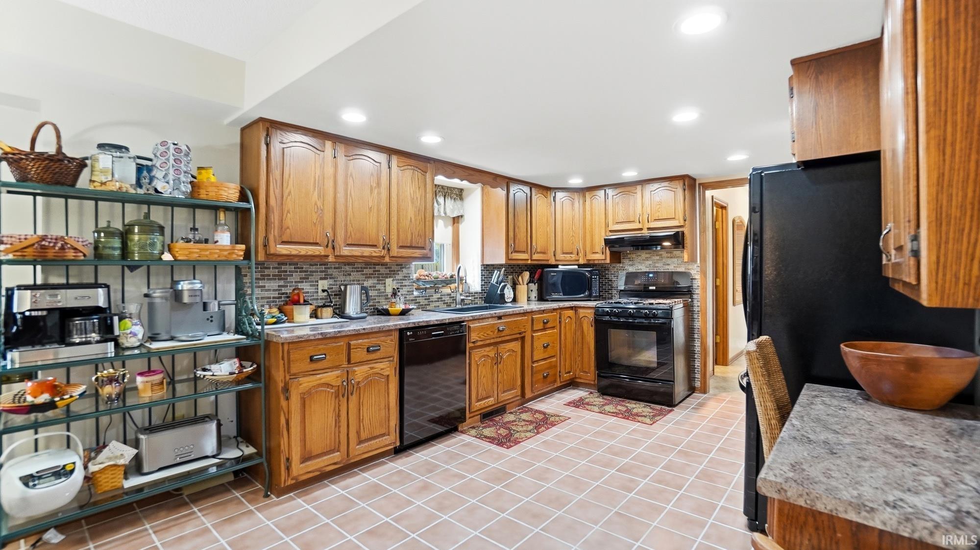 Kitchen with wood finish cabinetry, black appliances, light countertops, open shelves, and backsplash