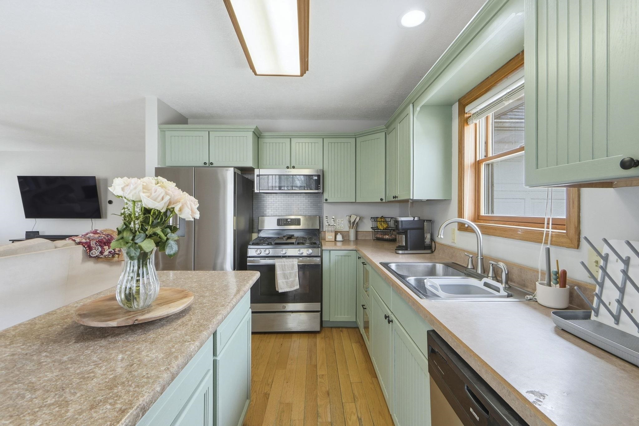 Kitchen with green cabinetry, stainless steel appliances, light countertops, light wood-type flooring, and recessed lighting