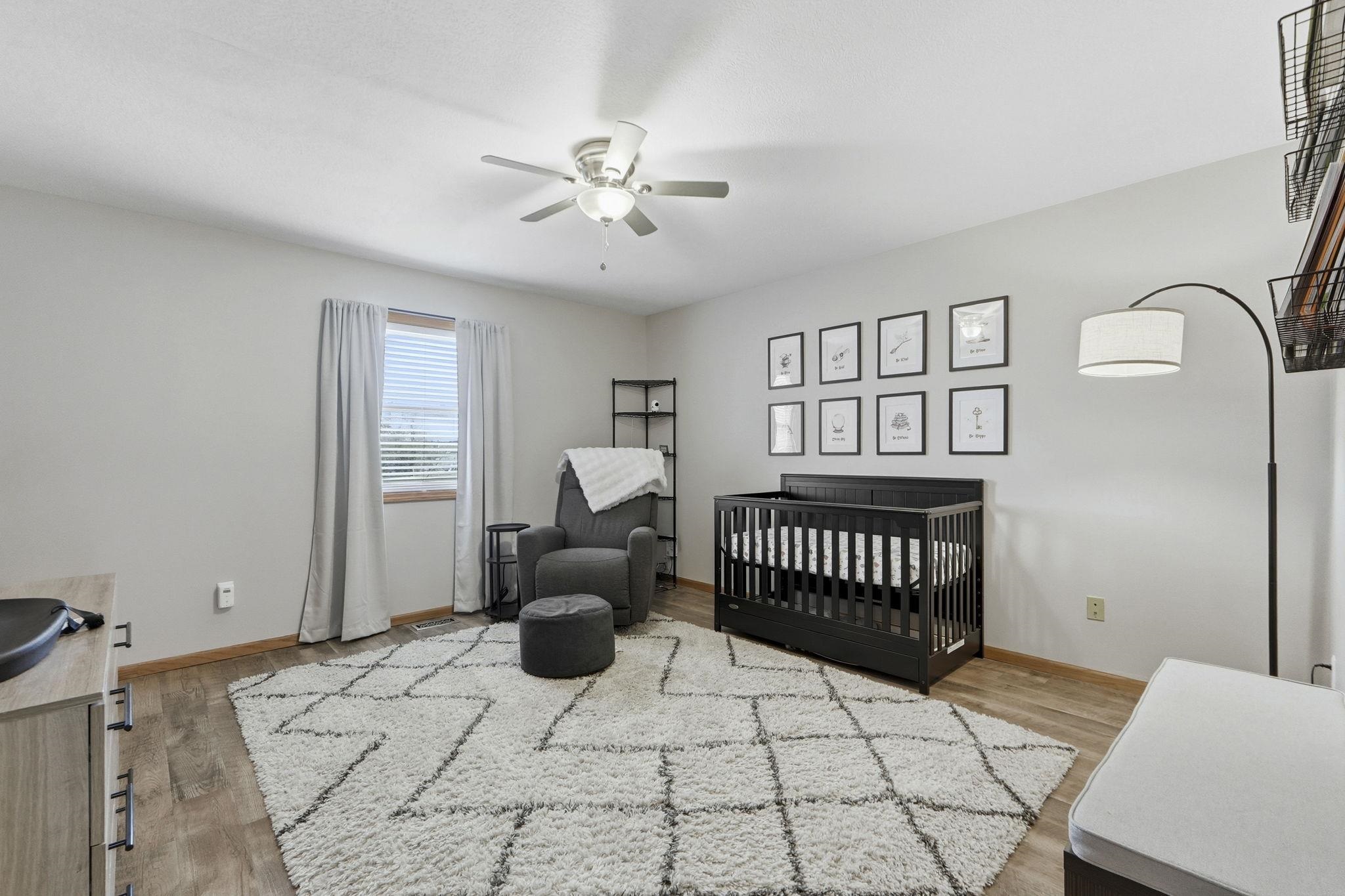 Bedroom featuring a crib, light wood-style flooring, and ceiling fan
