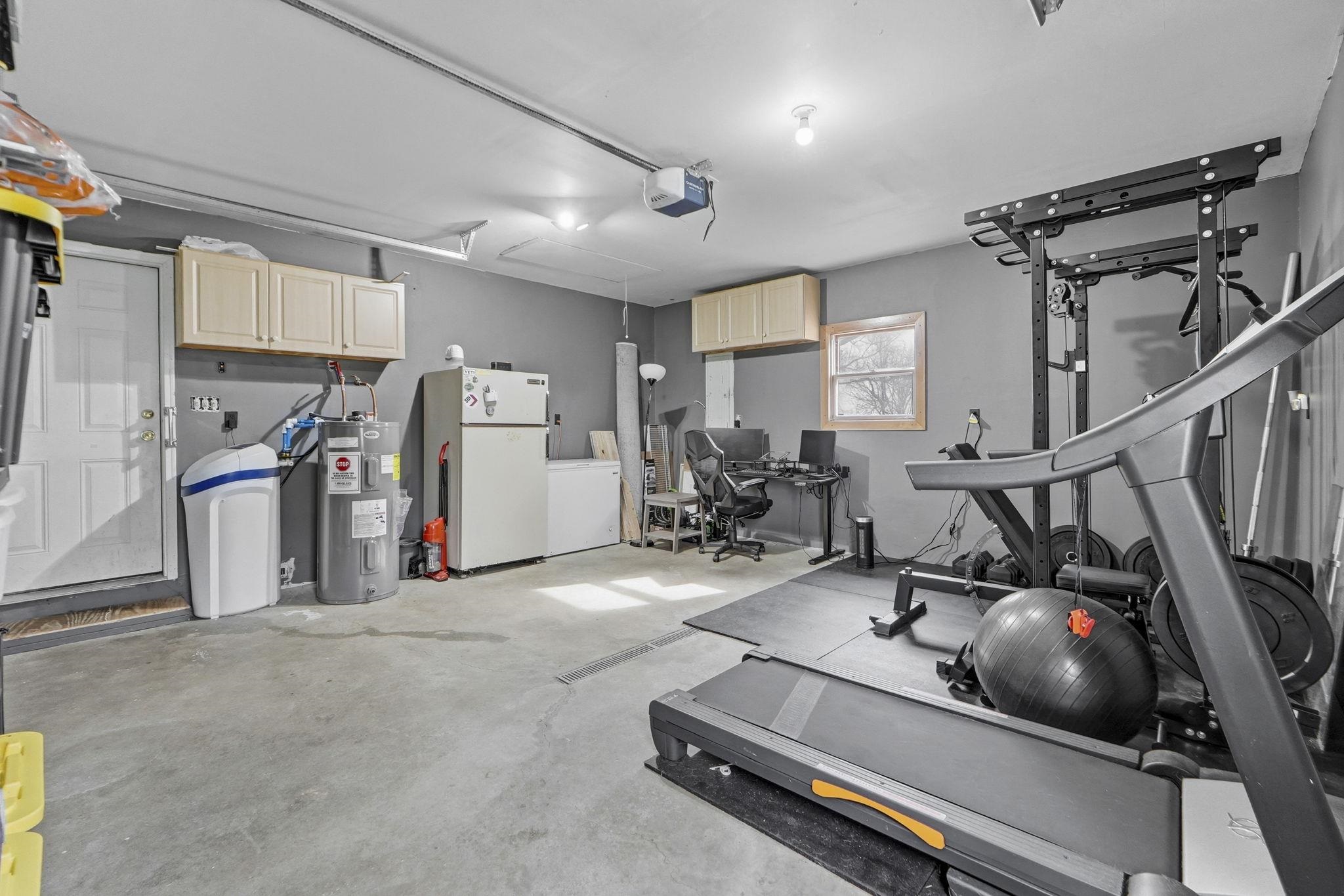 Workout area with a garage, electric water heater, and concrete floors