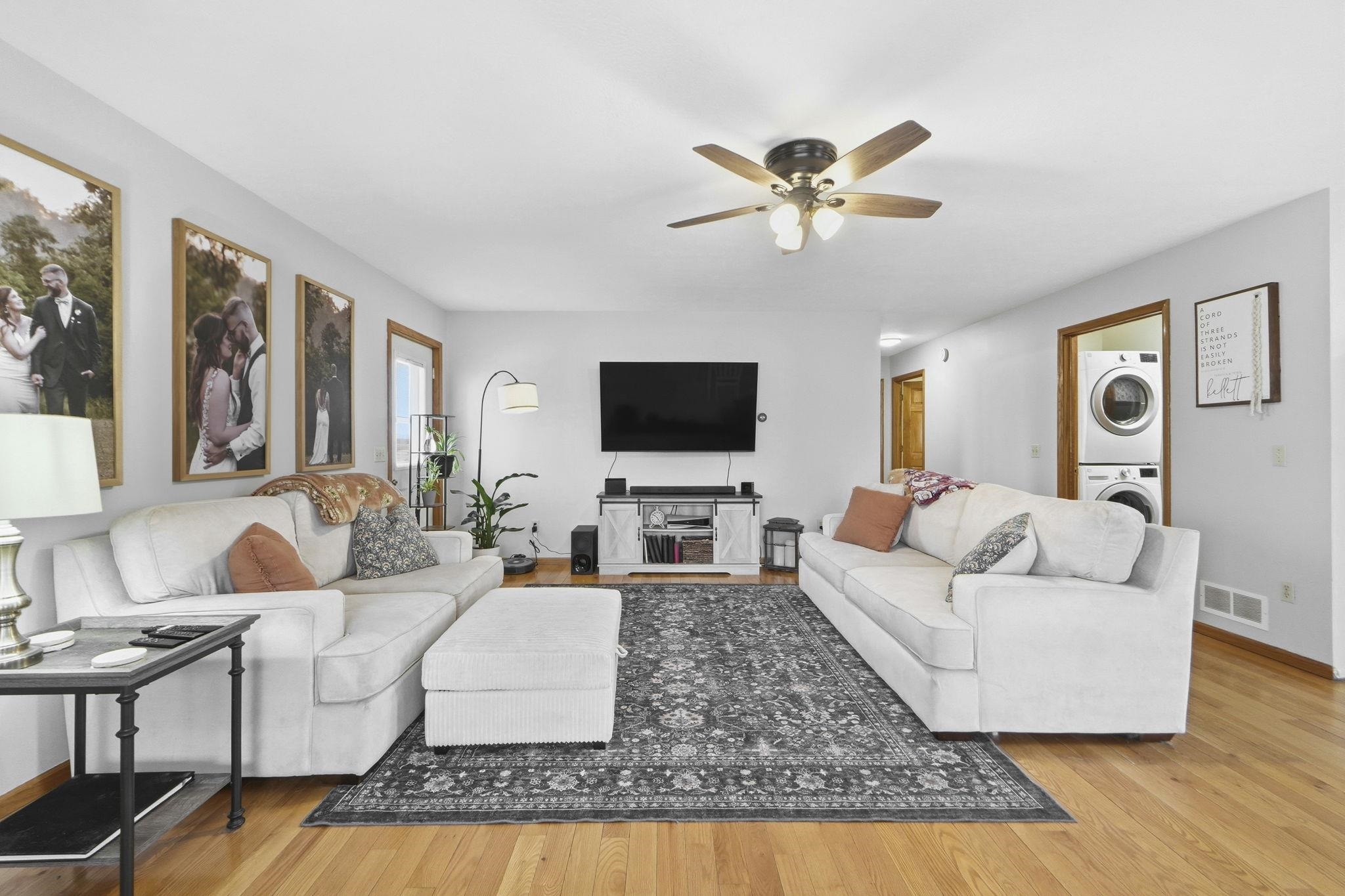 Living area with light wood finished floors, stacked washer and clothes dryer, and a ceiling fan