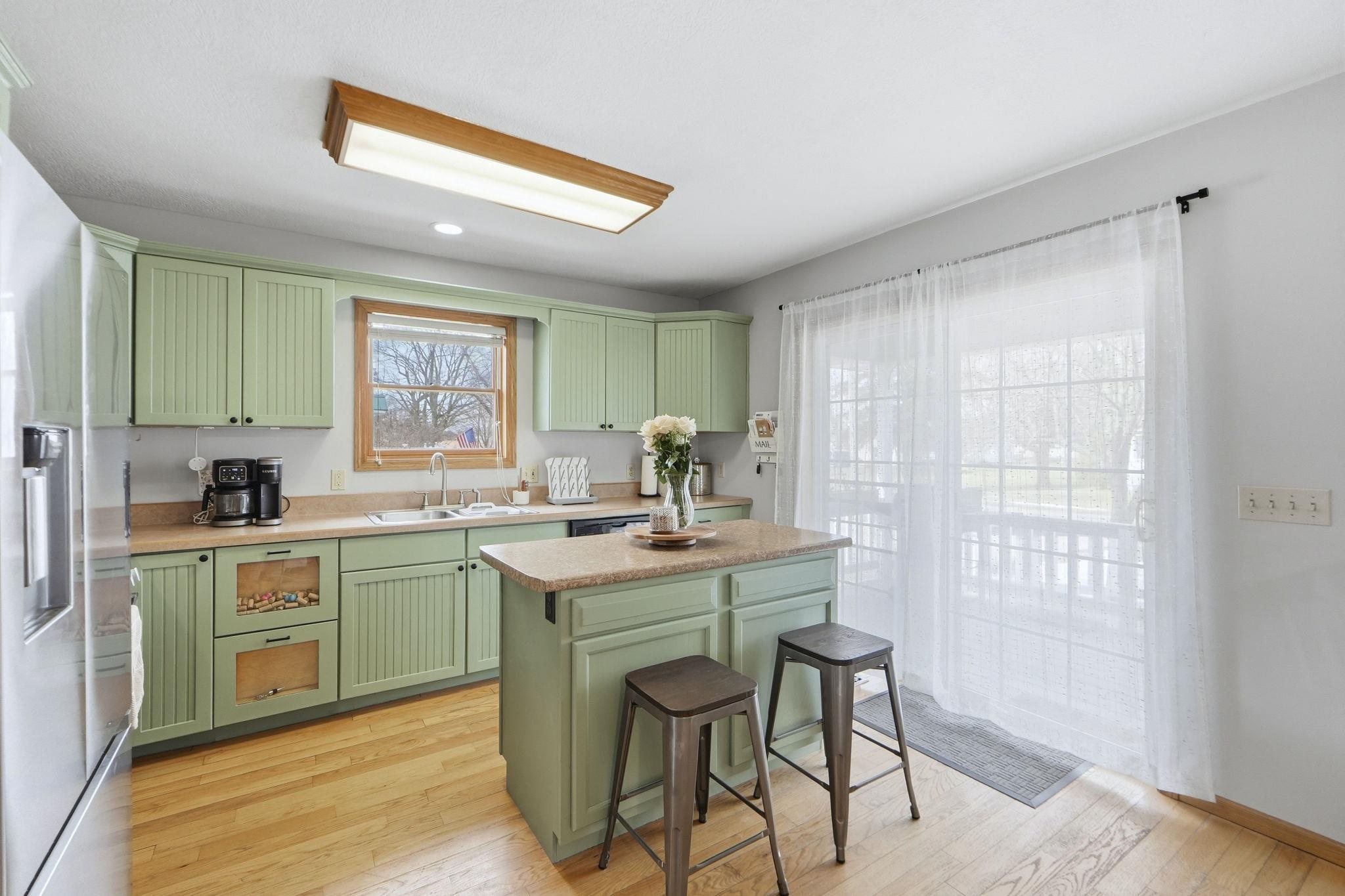 Kitchen with green cabinets, light countertops, stainless steel fridge, light wood finished floors, and recessed lighting